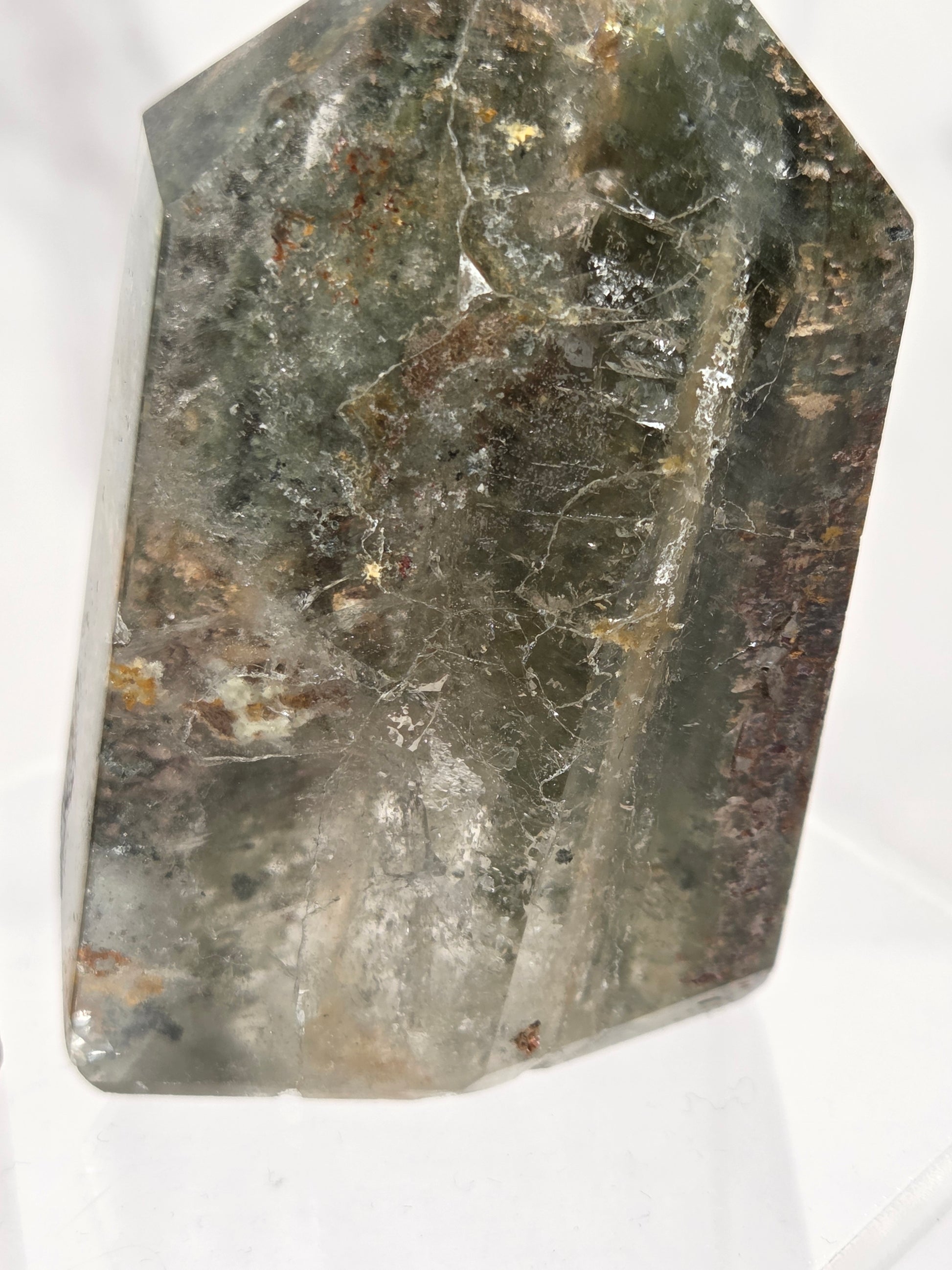 A natural clear quartz crystal with prominent green and brown inclusions, photographed on a white background.