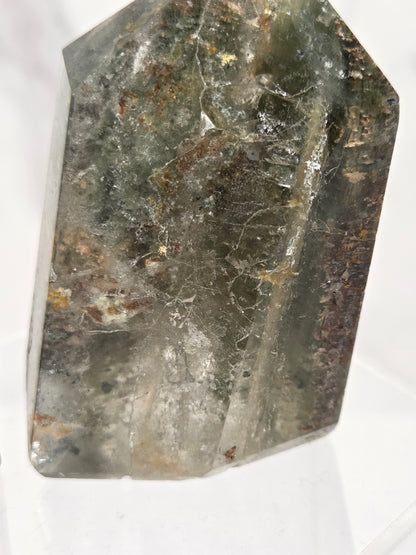 A natural clear quartz crystal with prominent green and brown inclusions, photographed on a white background.