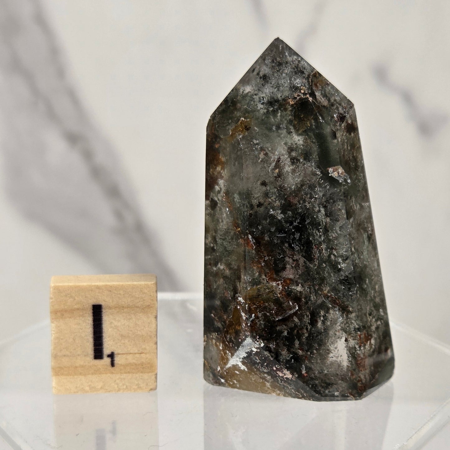 A natural pointed crystal or mineral specimen with a smoky gray and dark brown marbled pattern, displayed next to a small wooden block with the number 1 on a clear acrylic stand.