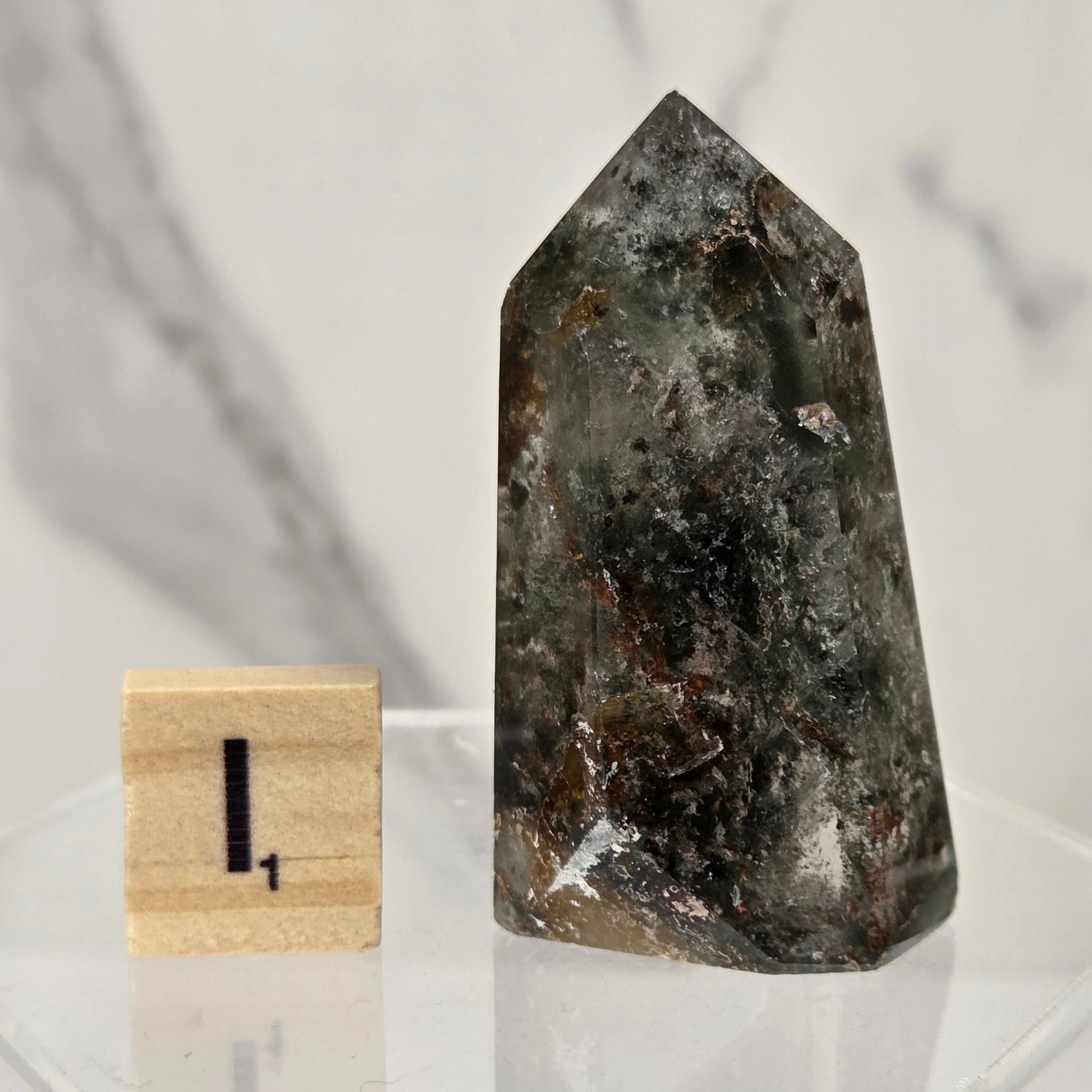 A natural pointed crystal or mineral specimen with a smoky gray and dark brown marbled pattern, displayed next to a small wooden block with the number 1 on a clear acrylic stand.