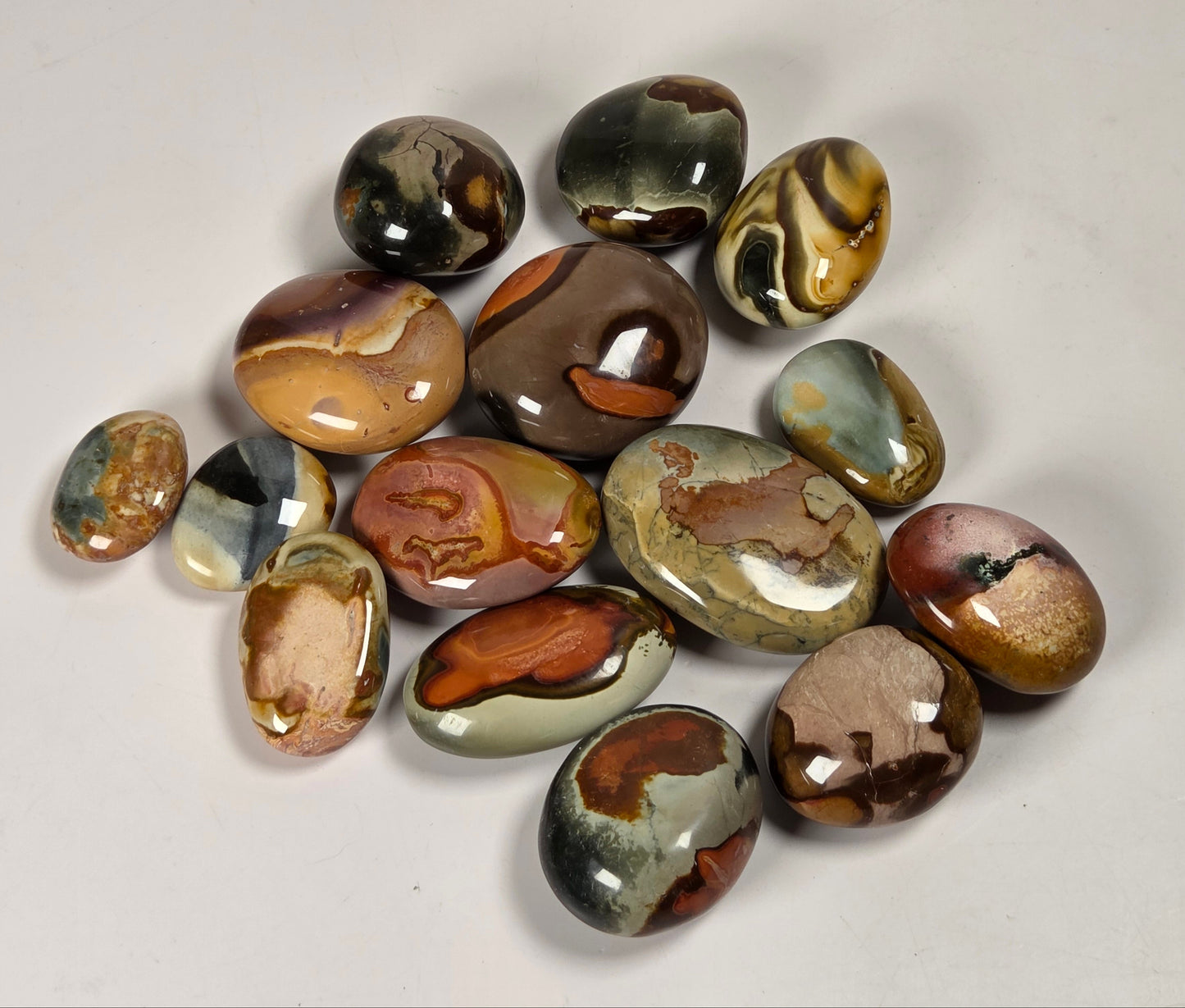 A group of polished agate stone cabochons in various earthy colors and patterns, arranged on a light gray background.