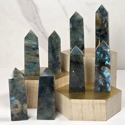 Seven polished labradorite crystal points of varying heights arranged on light wood and brass display blocks against a white marble background.