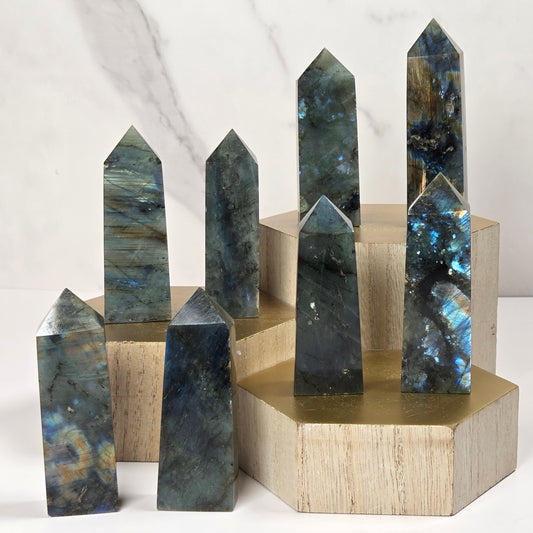 Seven polished labradorite crystal points of varying heights arranged on light wood and brass display blocks against a white marble background.