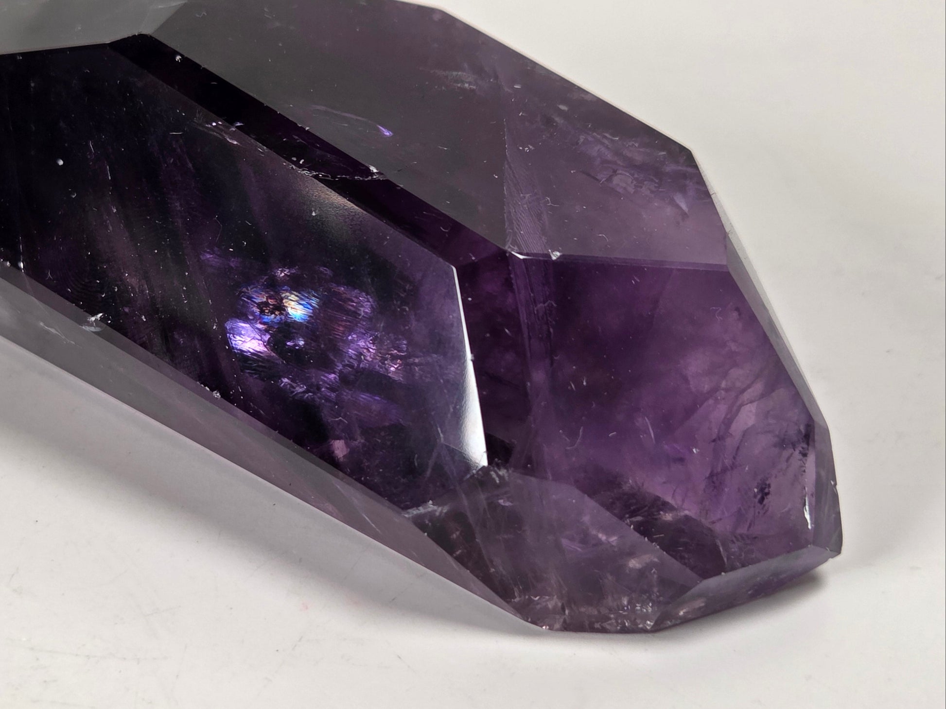 A faceted purple amethyst crystal point resting on a plain white surface.