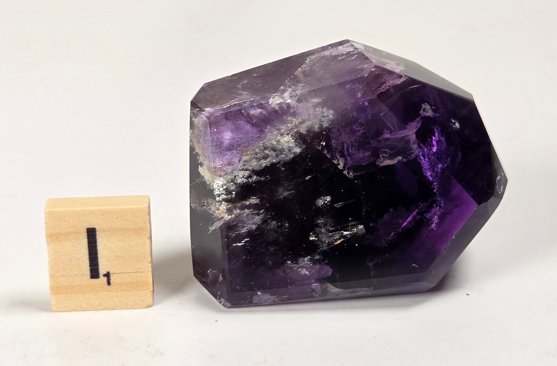 A faceted purple amethyst crystal stone displayed next to a small wooden block with the number 1 on a plain white surface.