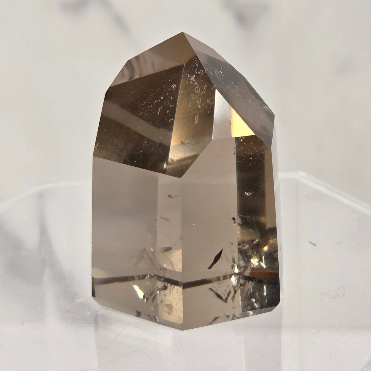 A natural clear quartz crystal point with internal inclusions, displayed on a clear acrylic stand against a light gray marble background.