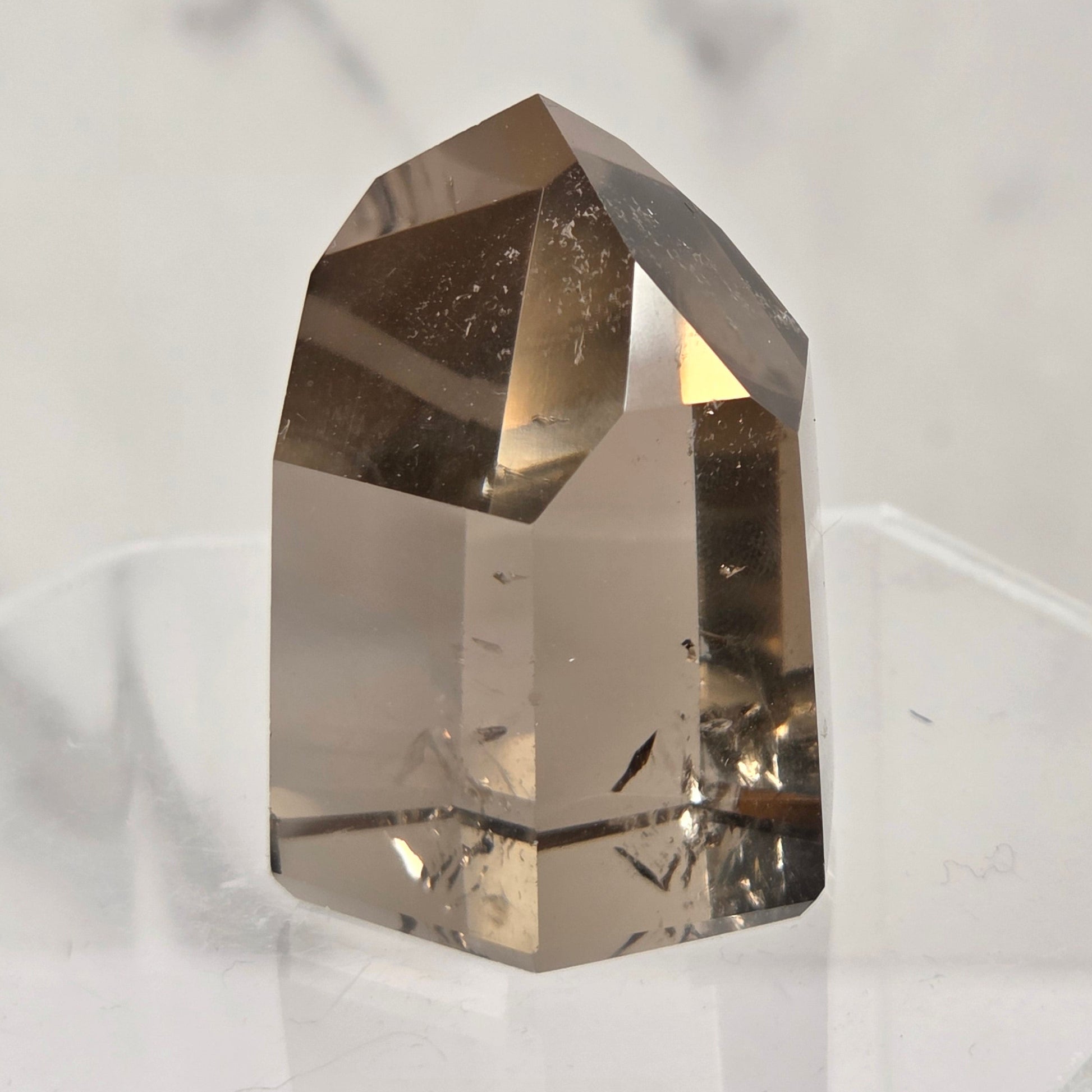 A natural clear quartz crystal point with internal inclusions, displayed on a clear acrylic stand against a light gray marble background.