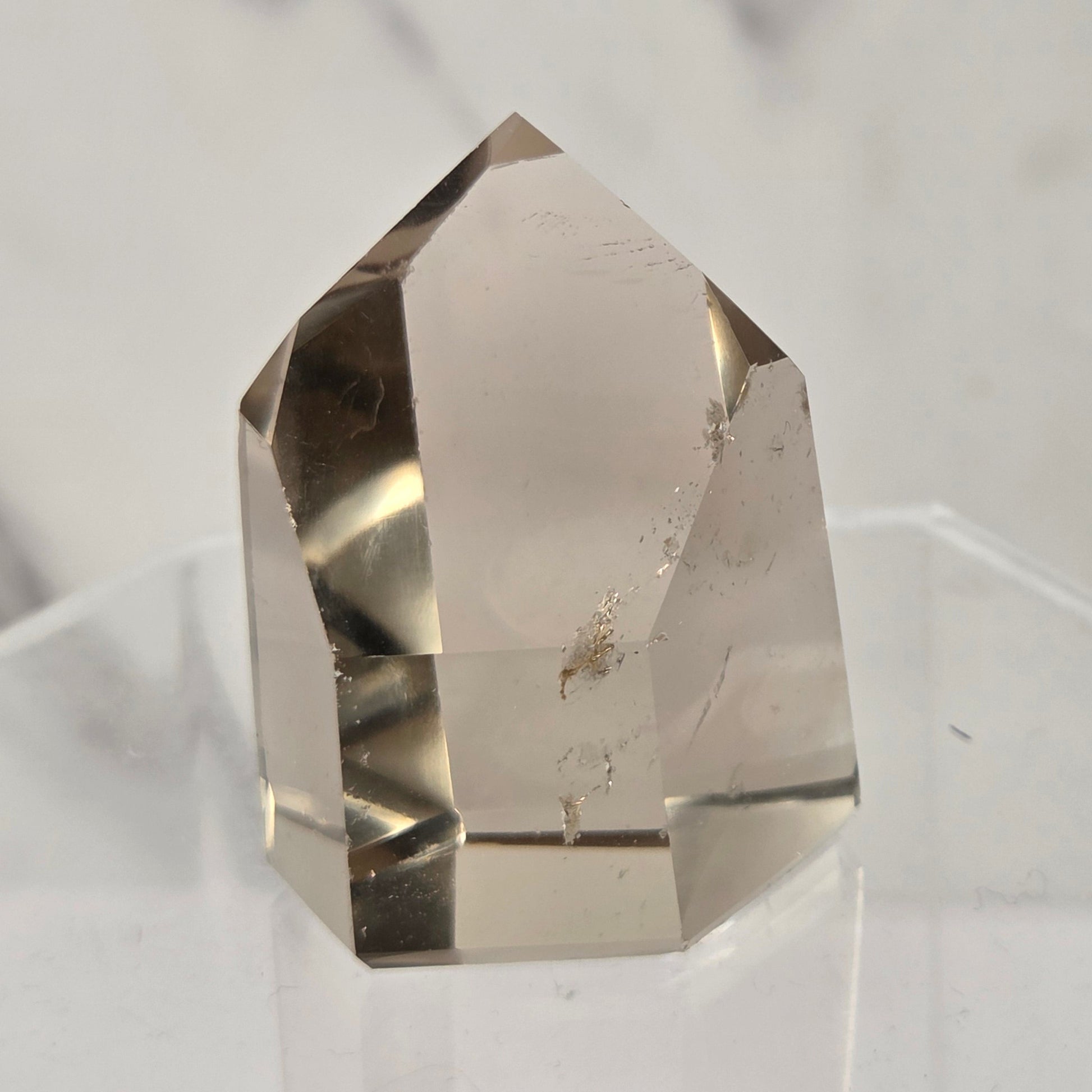 A natural clear quartz crystal point with internal inclusions, displayed on a clear acrylic stand against a light gray marble background.
