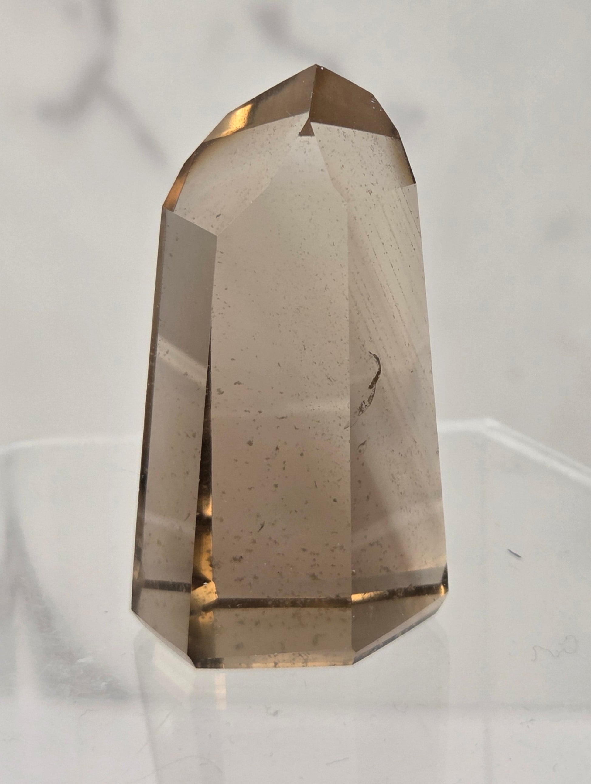 A faceted smoky quartz crystal tower displayed on a clear acrylic stand against a light gray marble-patterned background.