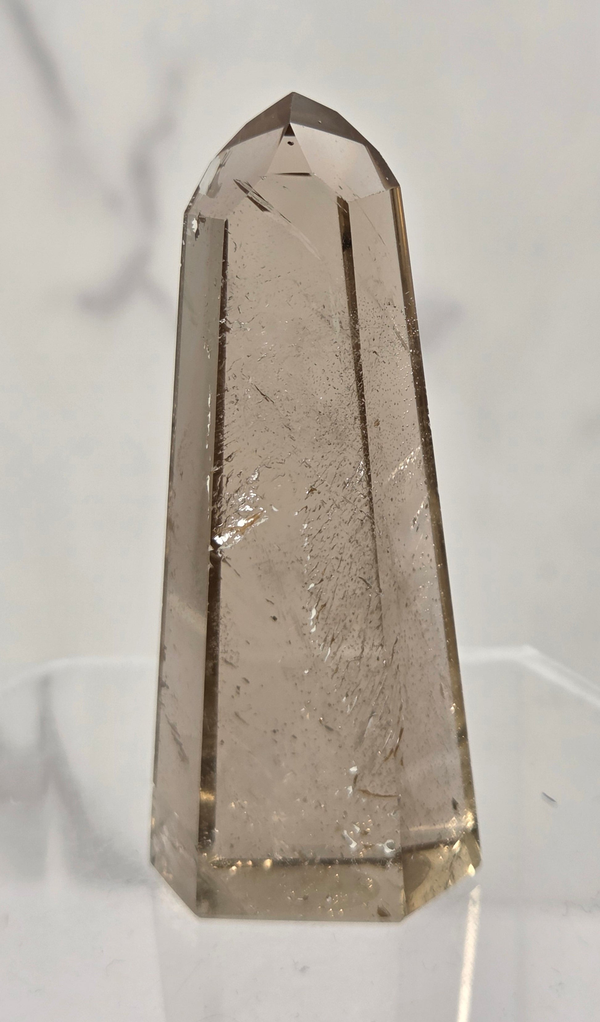 A faceted smoky quartz crystal tower on a clear acrylic display stand, set against a light gray marble-patterned background.