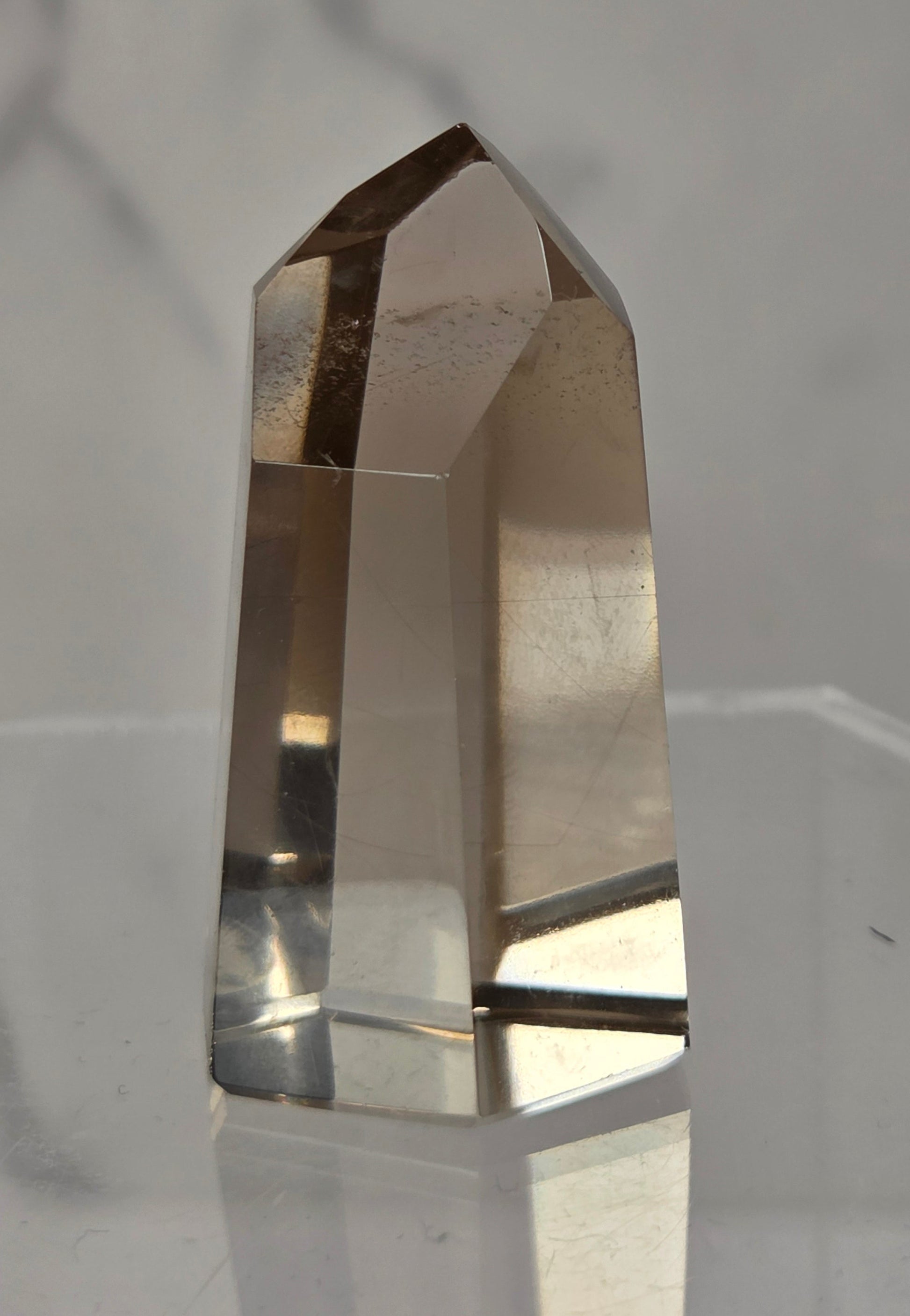 A natural smoky quartz crystal point tower displayed on a clear acrylic stand against a light gray marble-patterned background.