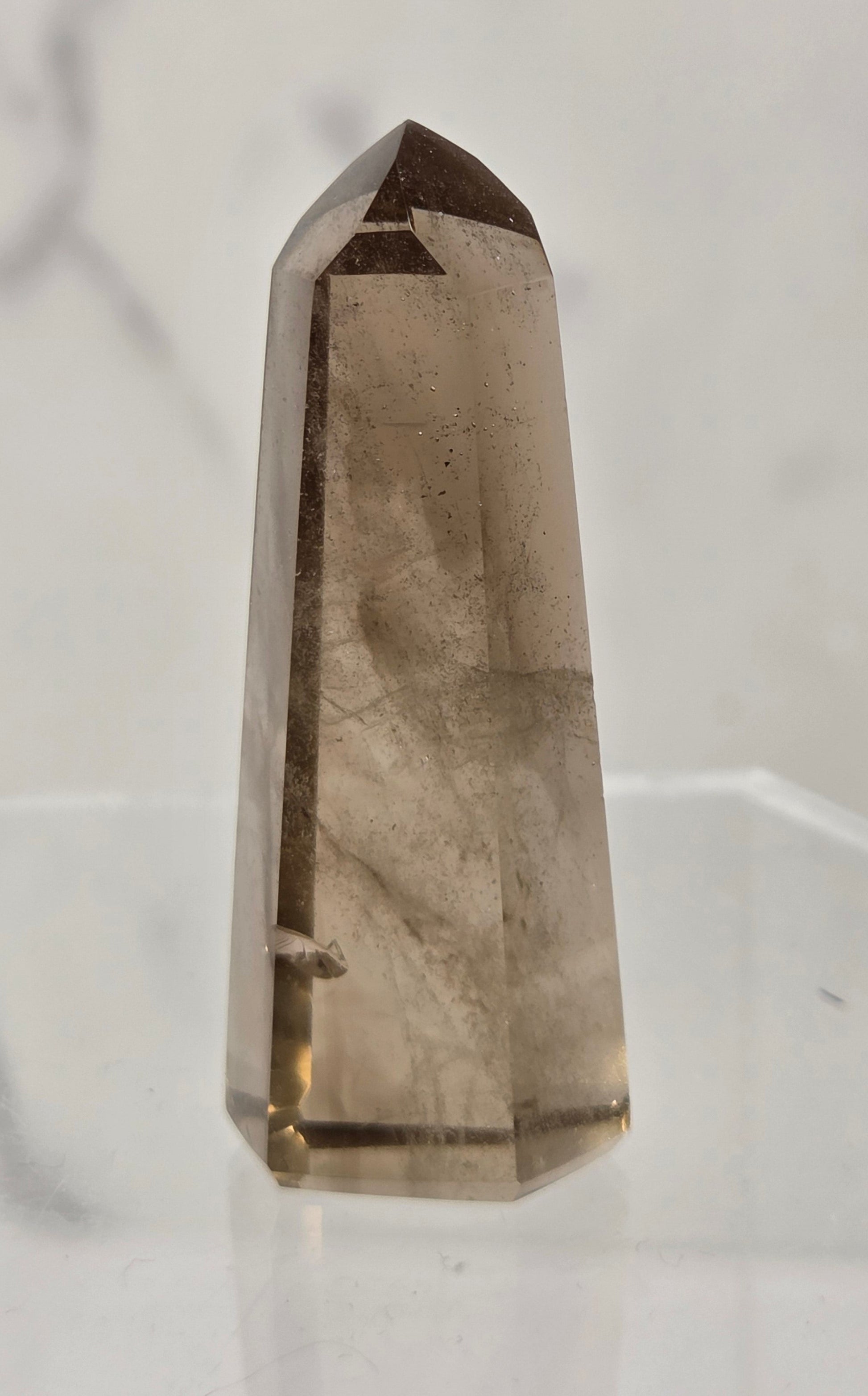 A natural smoky quartz crystal point tower standing upright on a clear acrylic display stand against a light gray marble-patterned background.