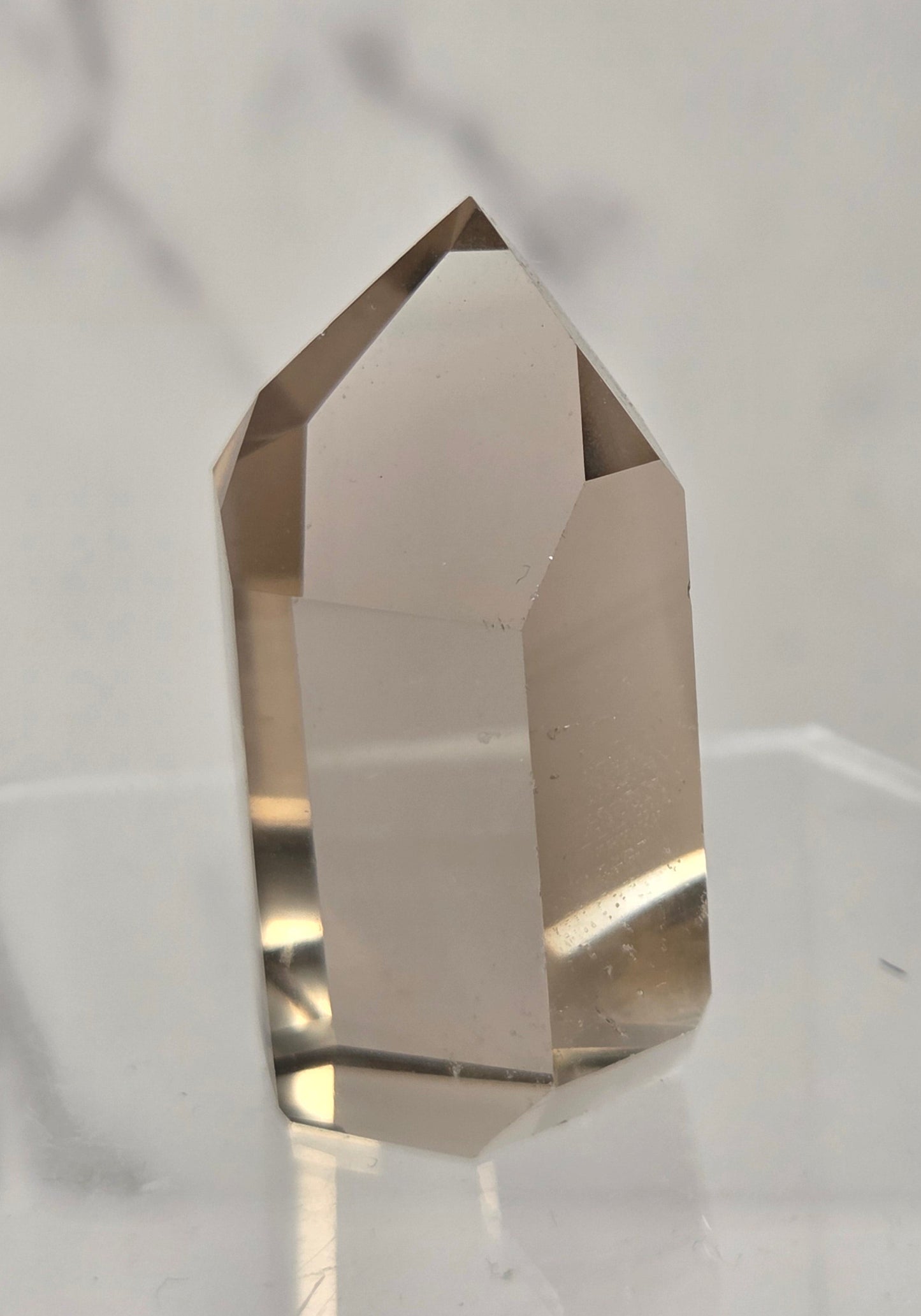 A faceted clear crystal point, likely quartz, standing upright on a transparent acrylic display stand against a light gray marble-patterned background.