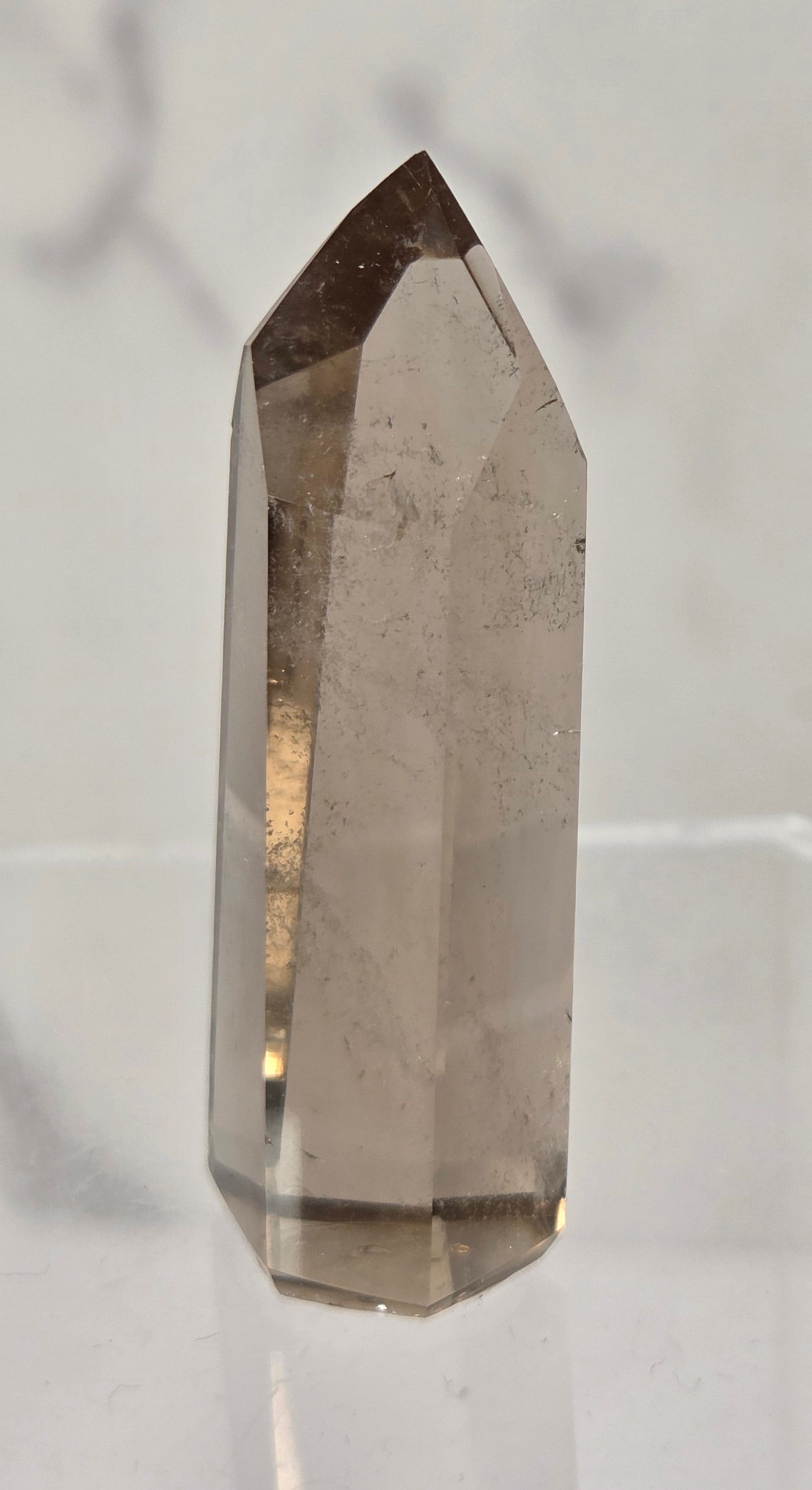 A natural smoky quartz point crystal standing upright on a clear acrylic display stand against a light gray marble-patterned background.