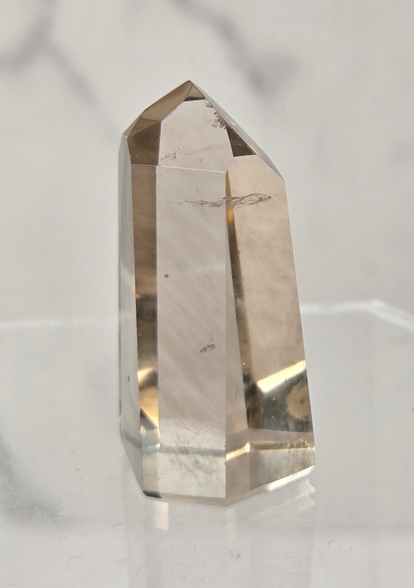 A natural smoky quartz crystal point with visible inclusions, displayed on a clear acrylic stand against a light gray marble background.