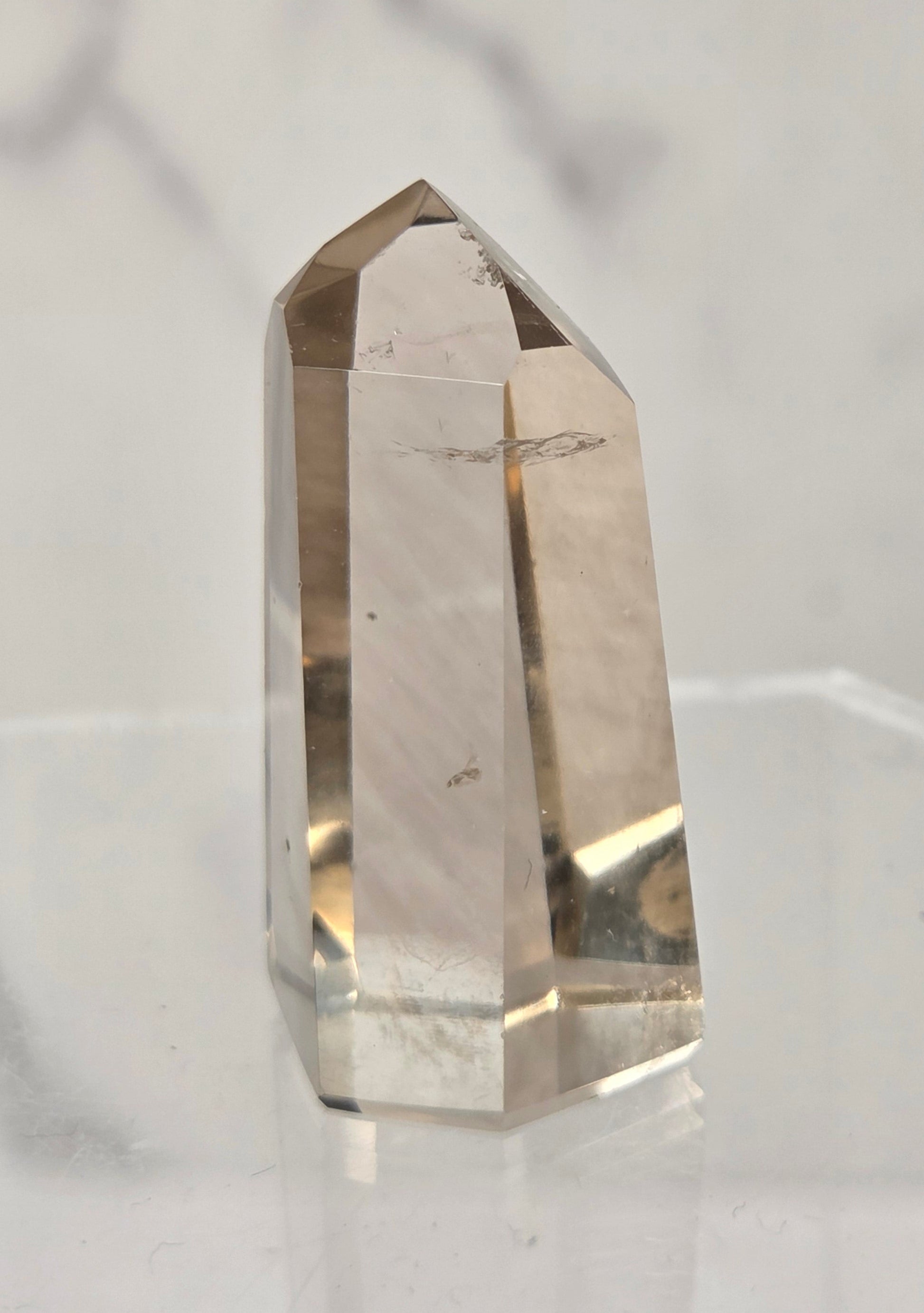 A natural smoky quartz crystal point with visible inclusions, displayed on a clear acrylic stand against a light gray marble background.