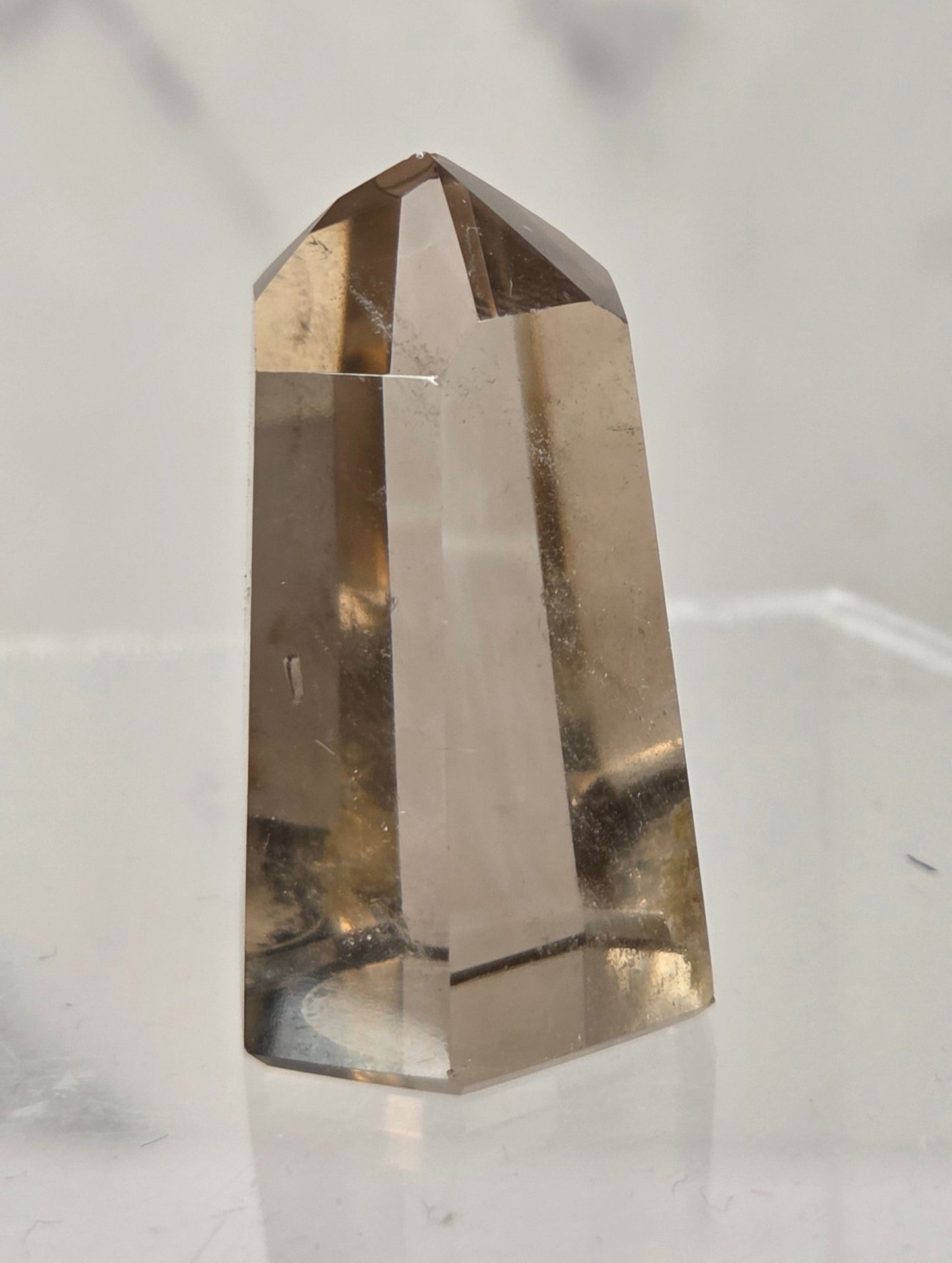 A natural smoky quartz crystal point displayed on a clear acrylic stand against a light gray marble background.