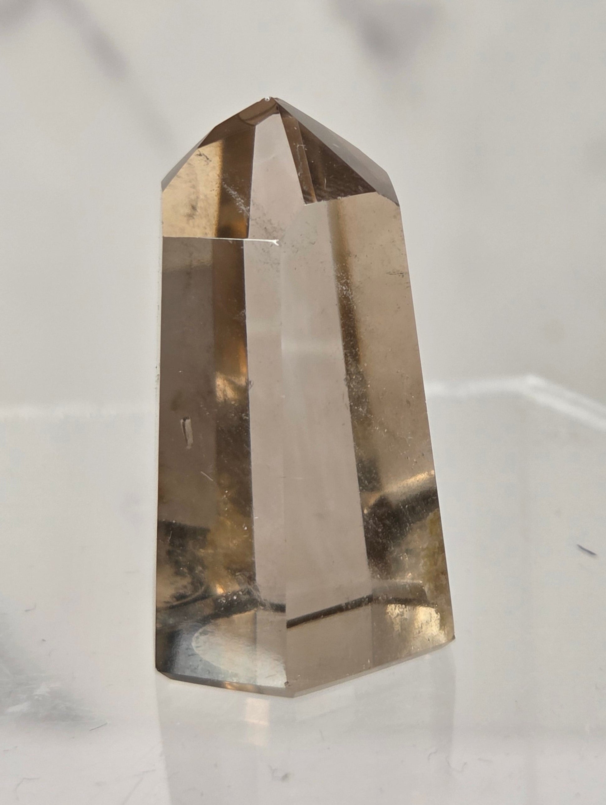 A natural smoky quartz crystal point displayed on a clear acrylic stand against a light gray marble background.