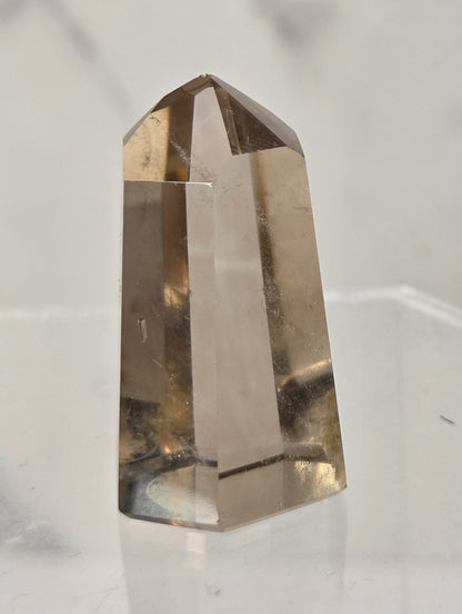 A natural smoky quartz crystal point displayed on a clear acrylic stand against a light gray marble background.