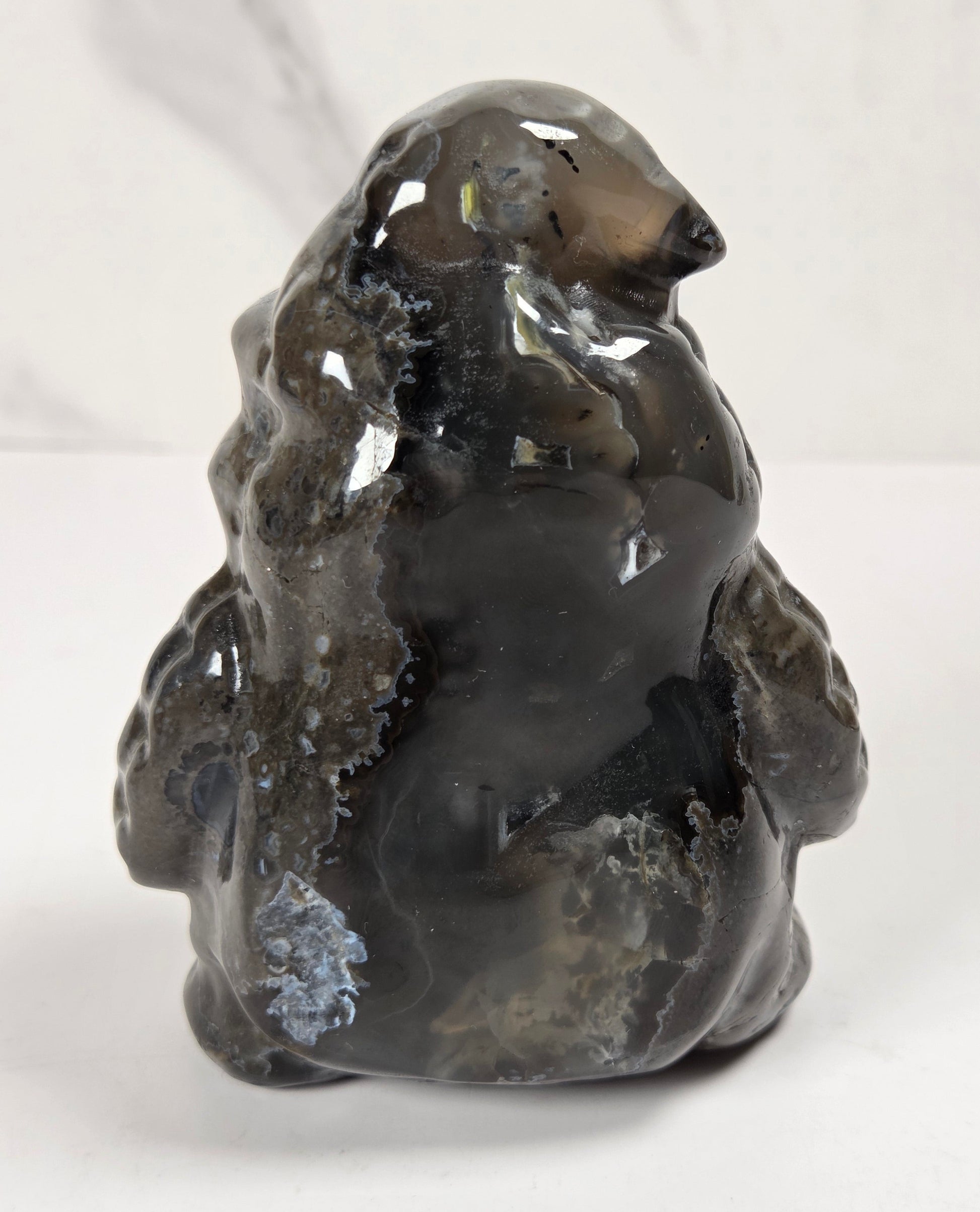 A polished dark gray agate stone figurine shaped like a polar bear, displayed on a white surface against a light gray marble-patterned background.