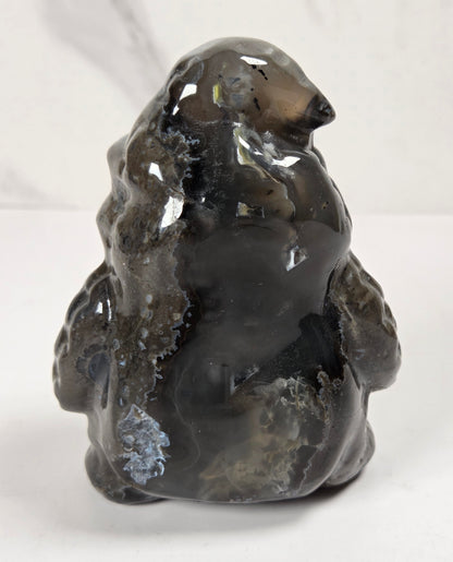A polished dark gray agate stone figurine shaped like a polar bear, displayed on a white surface against a light gray marble-patterned background.