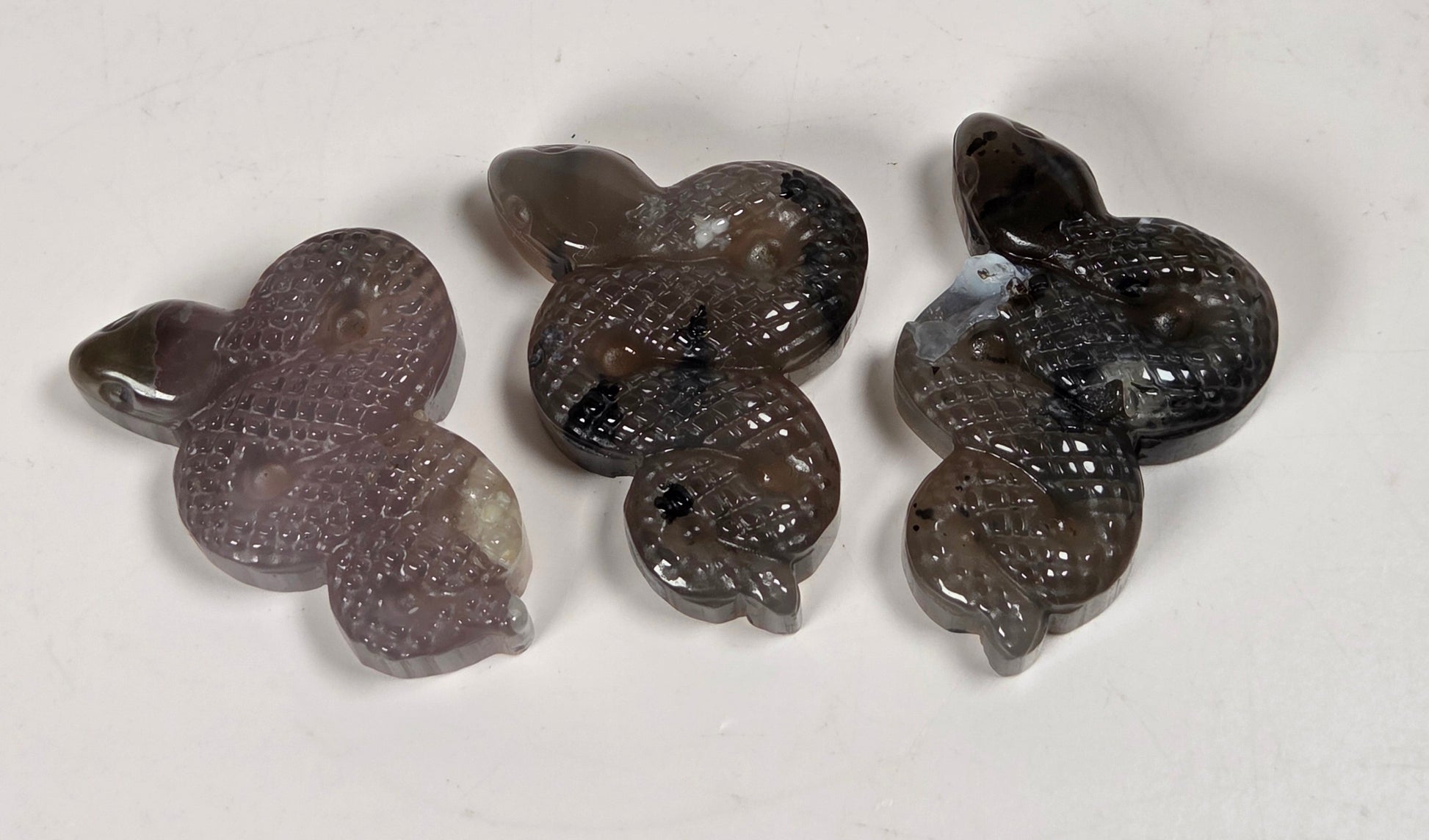 Three small carved stone beads or pendants with a textured, organic shape, arranged vertically on a plain off-white surface. The beads transition from a translucent smoky gray at the top to a darker, almost black marbled pattern at the bottom.