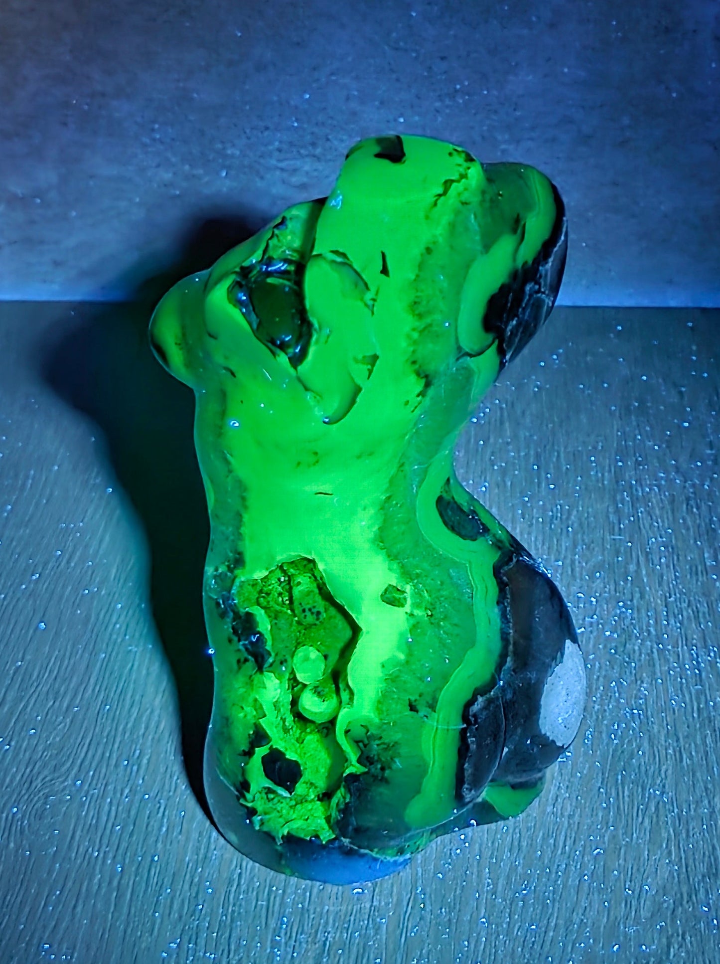 A glowing green and black decorative stone or crystal cluster, photographed on a dark surface with blue ambient lighting against a dark background.