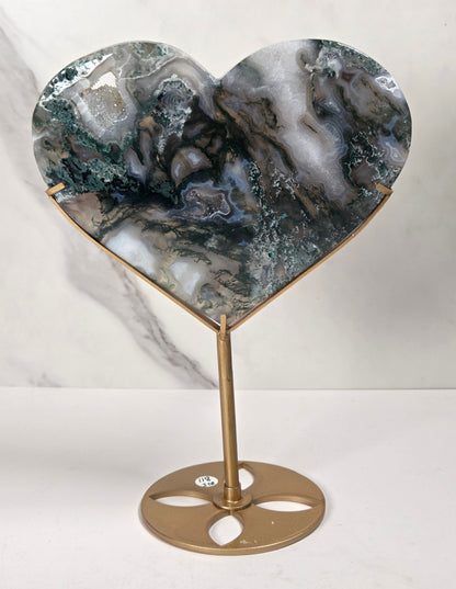 Heart-shaped tabletop carving with a polished agate stone face in green, gray, and white marbled patterns, mounted on a gold-finished metal stand with a circular base.