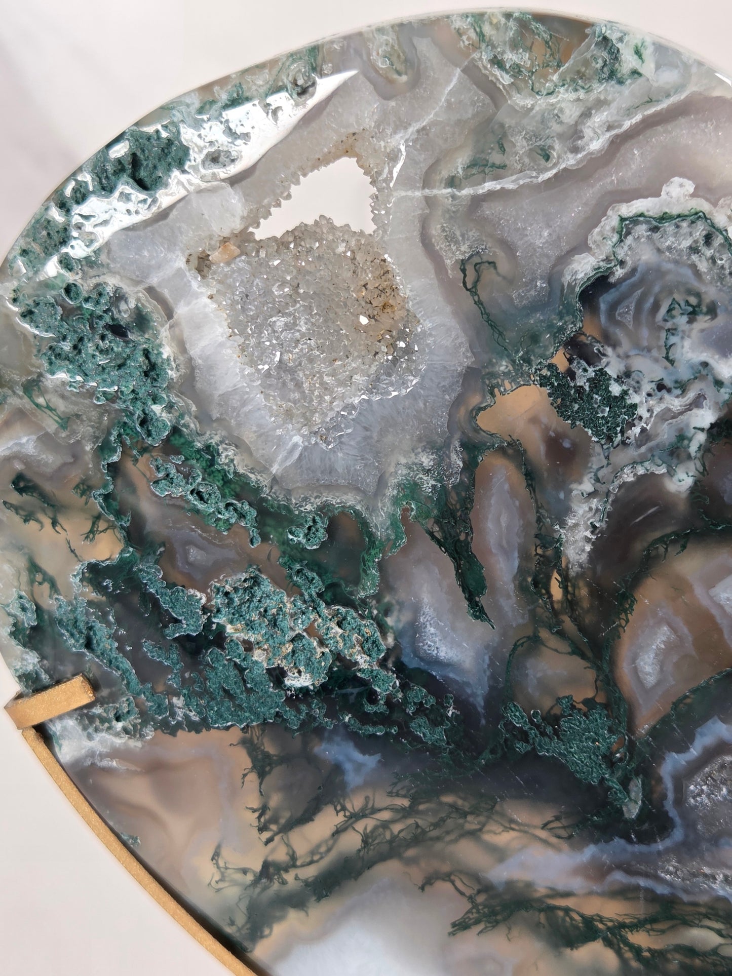 A close-up of a circular agate or geode-style wall art piece with layered natural stone patterns in teal, gray, white, taupe, and brown, mounted on a light wood frame.