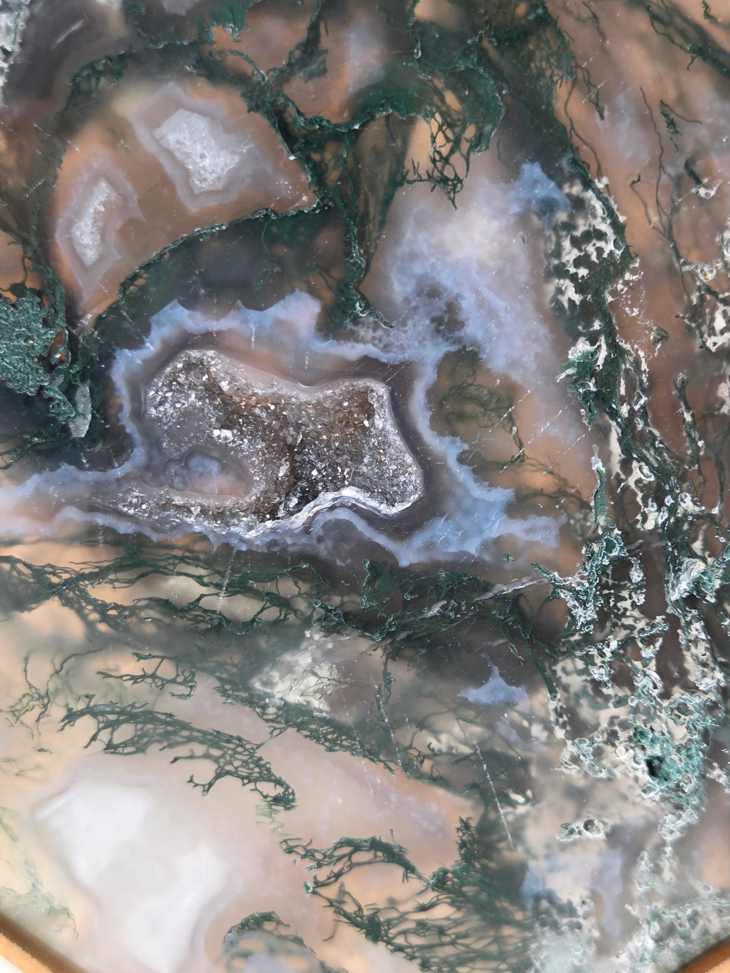 A close-up of a polished agate or geode-style stone slab with swirling bands of brown, gray, white, pale blue, and dark green veining.