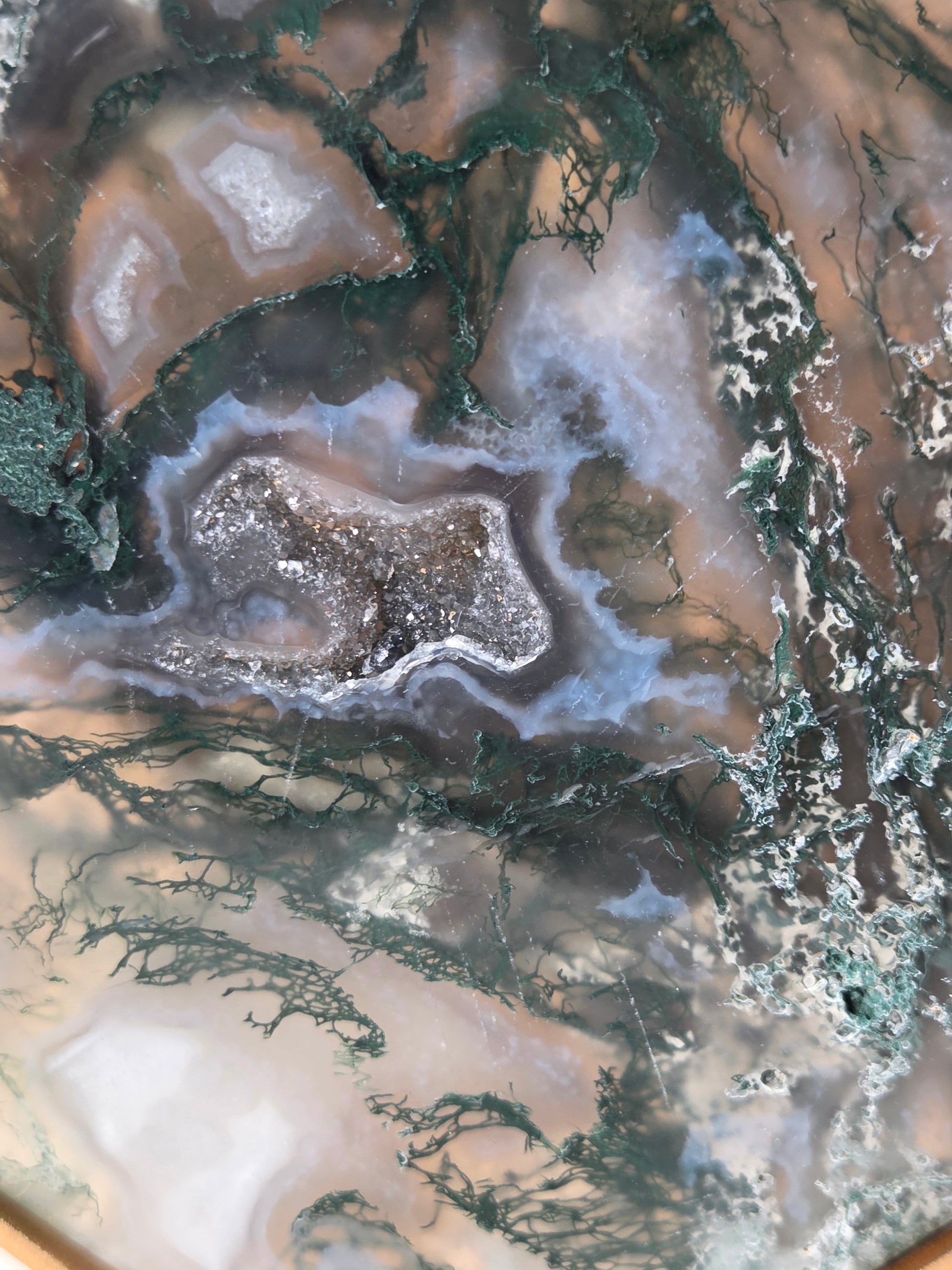 A close-up of a polished agate or geode-style stone slab with swirling bands of brown, gray, white, pale blue, and dark green veining.