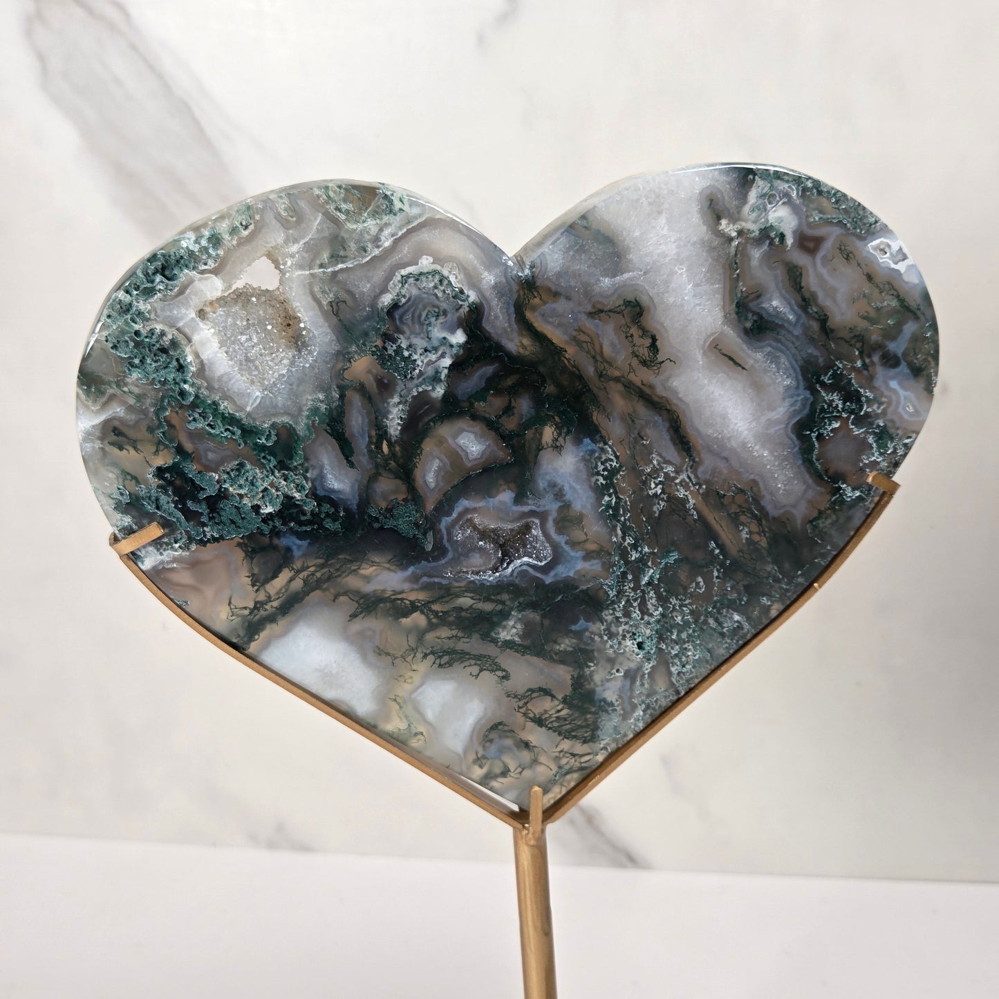 Heart-shaped agate geode resin sculpture on a gold metal stand, displayed against a white marble background.