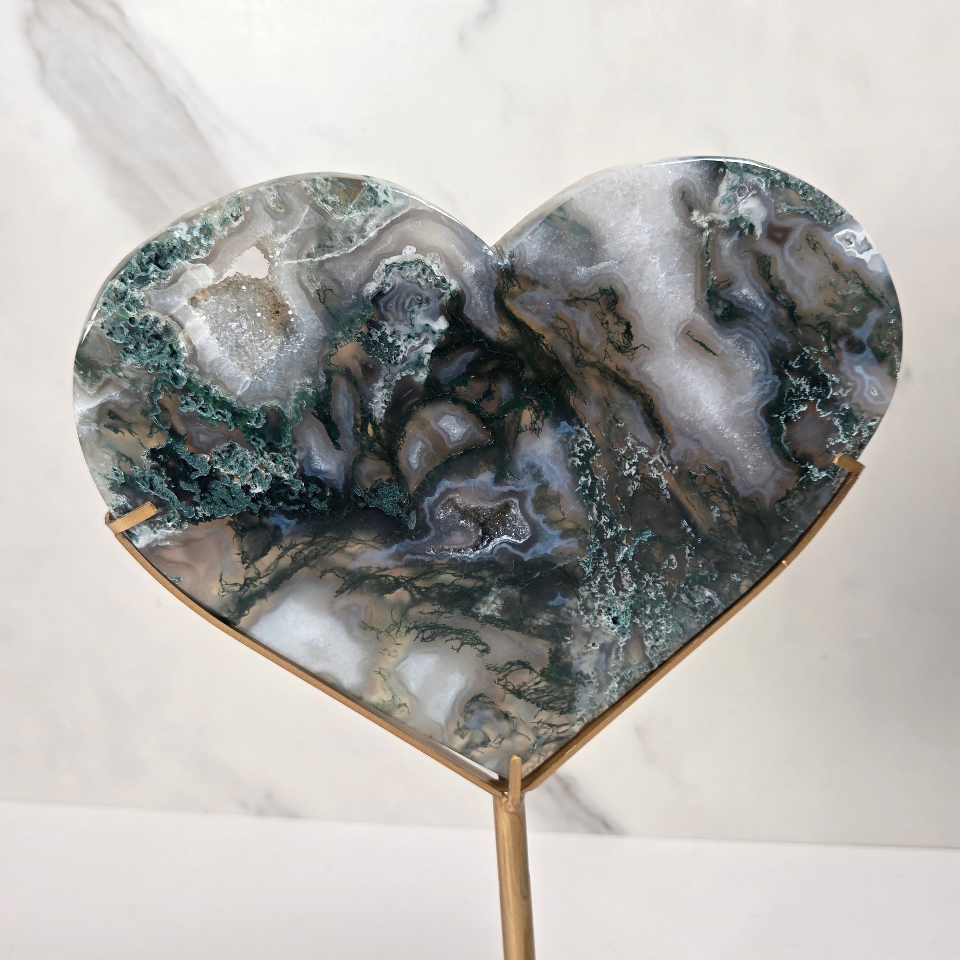 Heart-shaped agate geode resin sculpture on a gold metal stand, displayed against a white marble background.