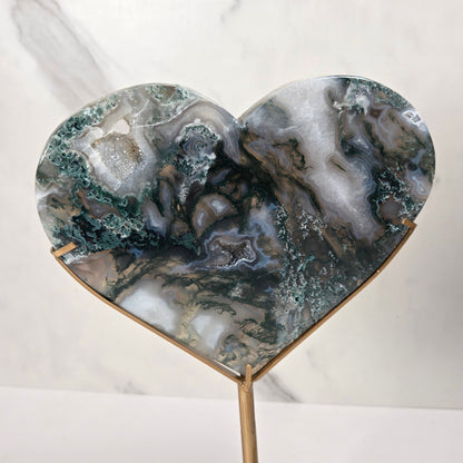 Heart-shaped agate geode resin sculpture on a gold metal stand, displayed against a white marble background.