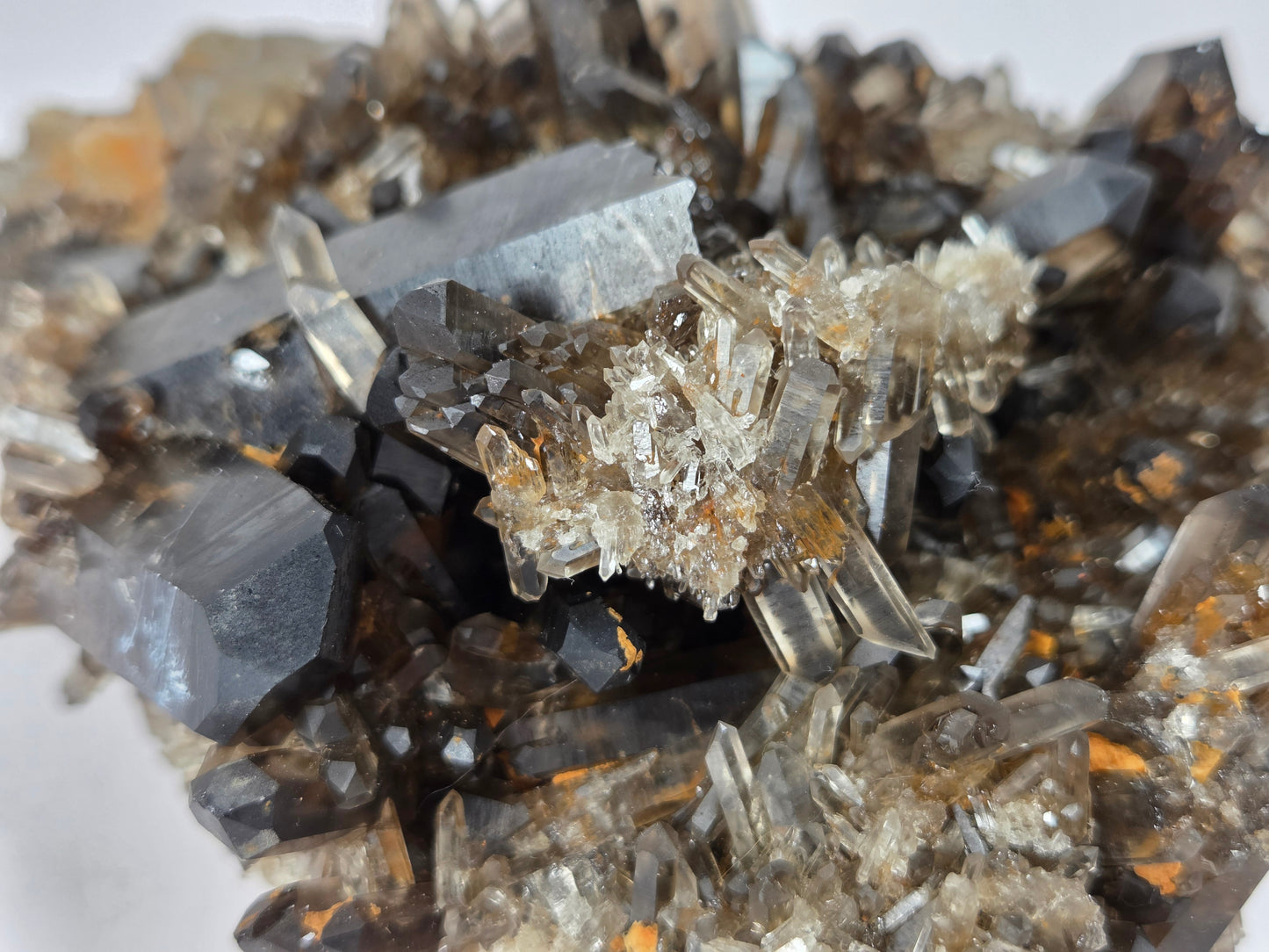 Close-up of a mineral specimen with dark gray to black tabular crystals and a central cluster of clear to smoky quartz-like crystals on a white background.
