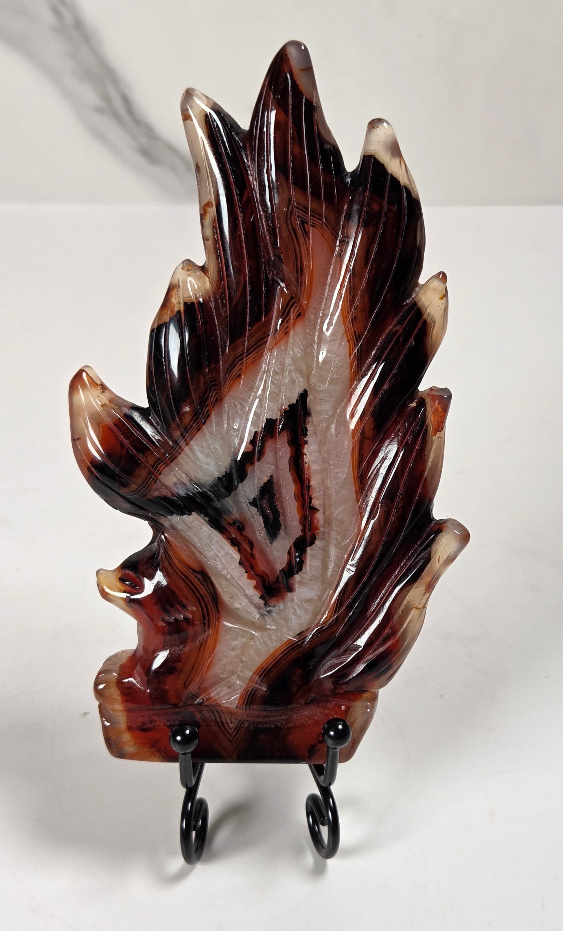 A carved agate flame-shaped sculpture displayed on a small black stand against a white and gray marble-patterned background.