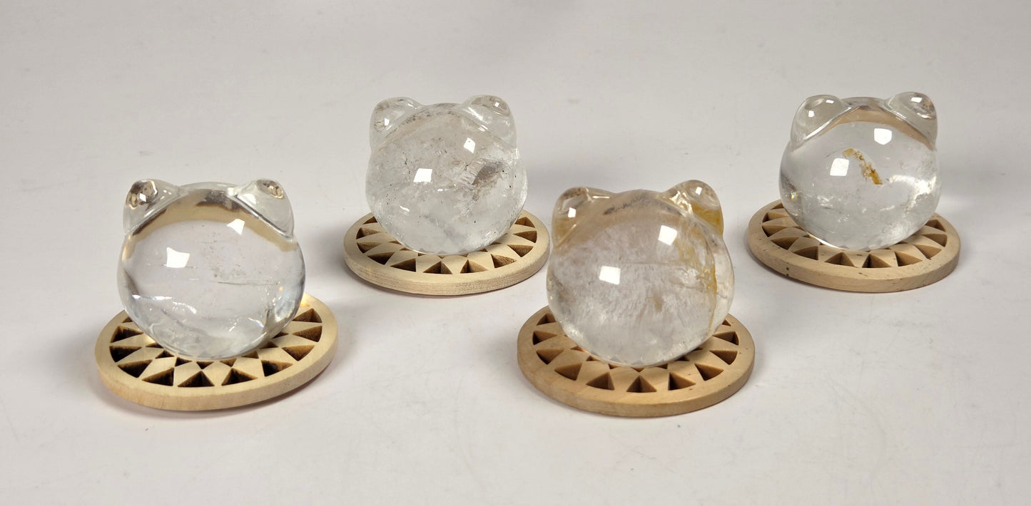 Four clear crystal cat figurines with gold-colored metal accents, each resting on a small round wooden base, arranged on a white surface.