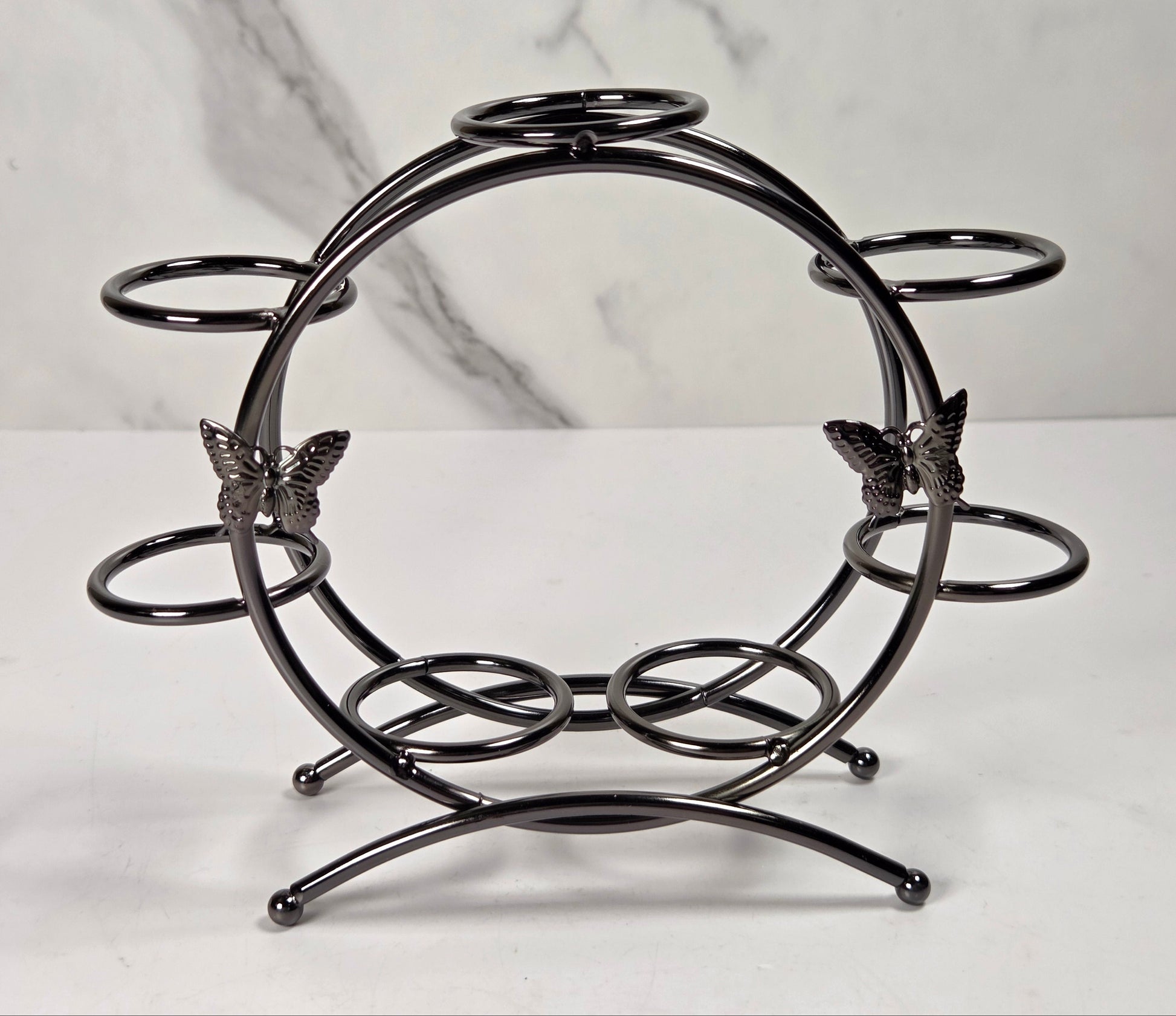 A black metal wine and glass holder with butterfly accents, displayed on a white marble surface against a white marble background.