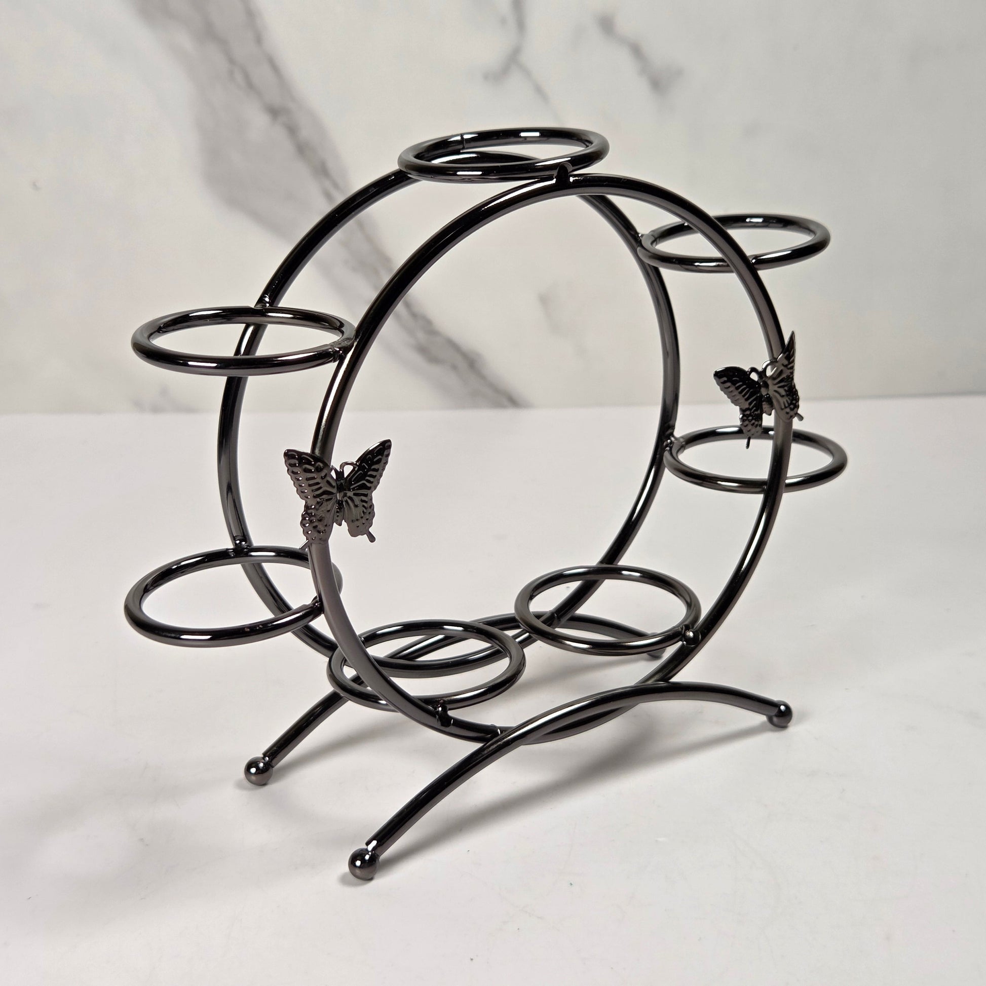 A black metal wine bottle holder with butterfly accents, displayed on a white marble surface against a white marble background.