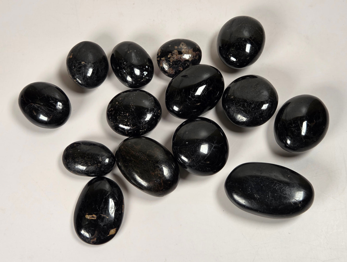 A group of polished black oval stones, likely tumbled obsidian or jasper chips, arranged on a plain off-white background.