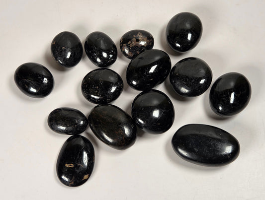 A group of polished black oval stones, likely tumbled obsidian or jasper chips, arranged on a plain off-white background.