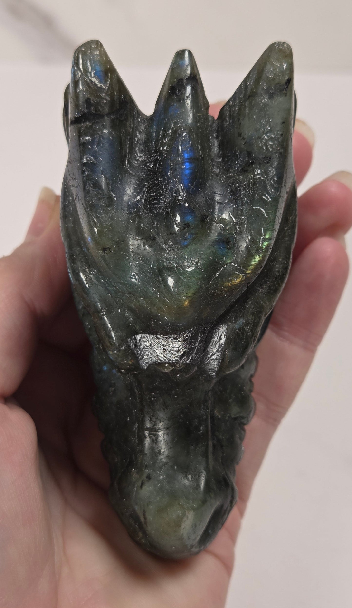 A hand holding a polished labradorite crystal carving shaped like a dragon head, showing its natural iridescent color shifts.