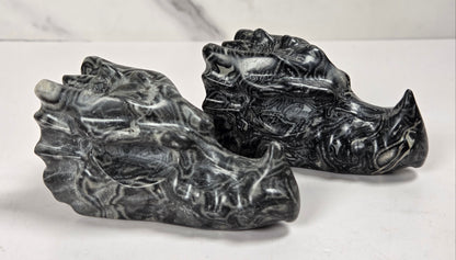 Two carved black and white stone dragon heads, likely made of marble or soapstone, displayed on a light marble surface.