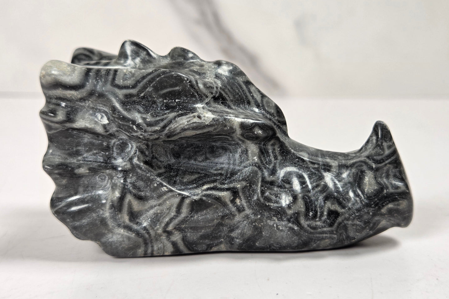 A carved stone sculpture of a dragon head, featuring black and gray marbled patterns, displayed on a light surface against a neutral background.