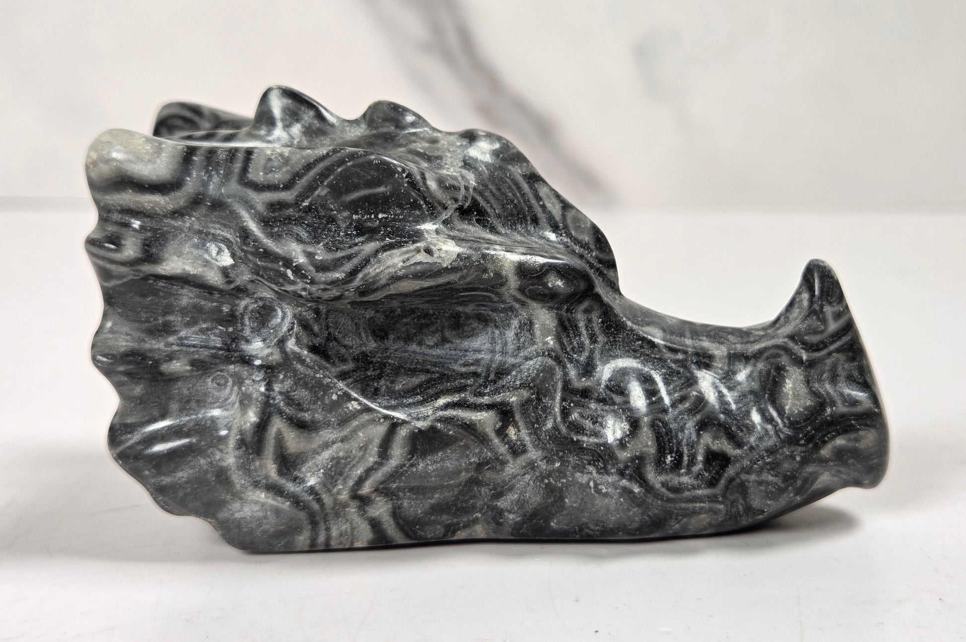 A carved stone sculpture of a dragon head, featuring black and gray marbled patterns, displayed on a light surface against a neutral background.