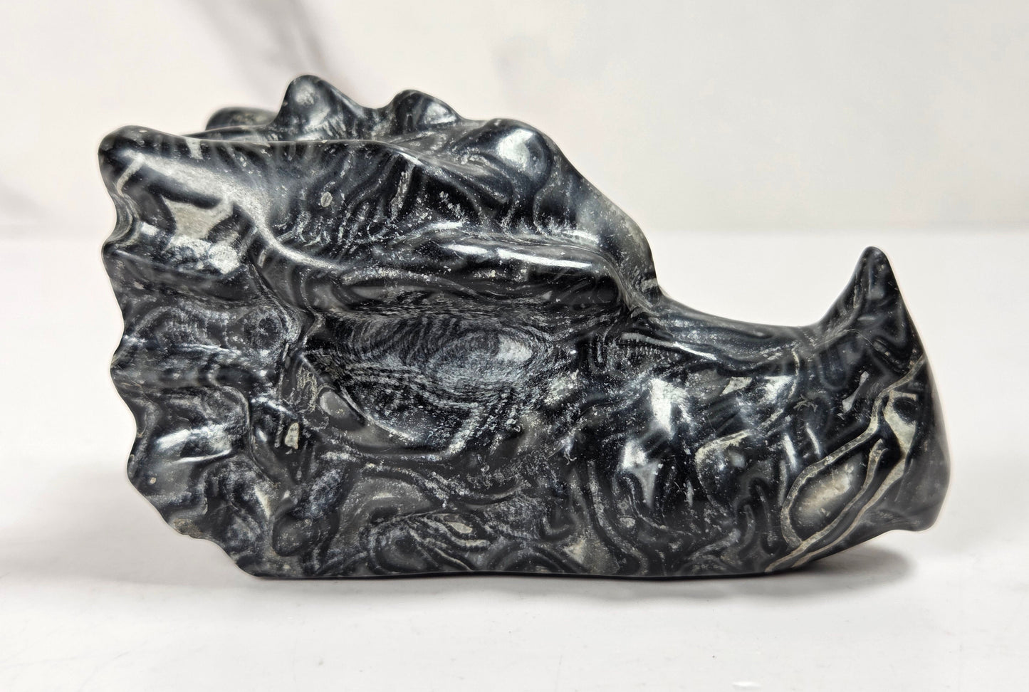 A polished black and white marbled stone object with a sculpted, organic surface, photographed on a light neutral background.