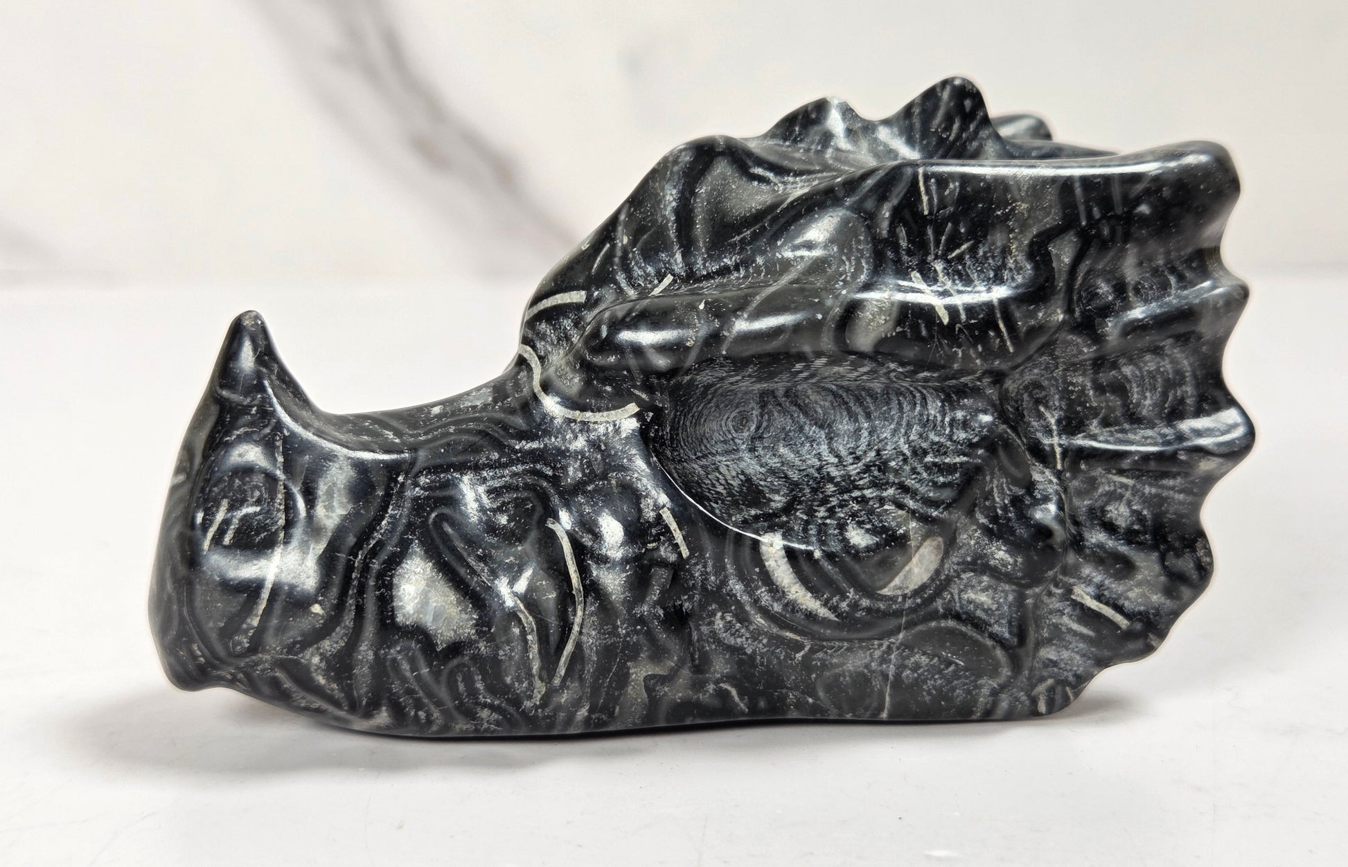 A carved black rhinoceros skull figurine made of polished stone, displayed on a light surface with a marble-patterned background.