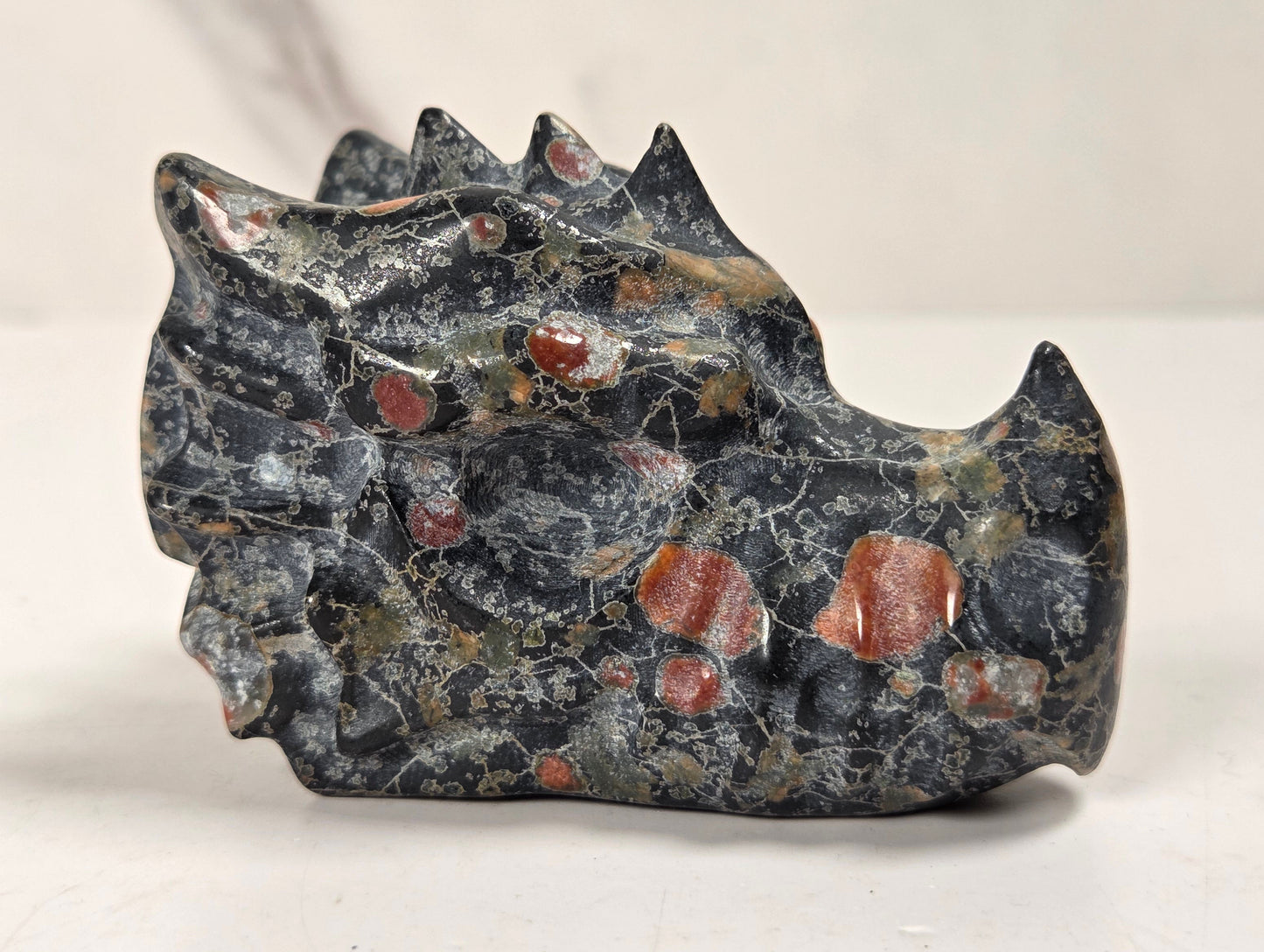 A carved stone object with a dark gray and black marbled texture and scattered reddish-orange inclusions, photographed on a light neutral surface.