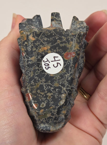 A hand holding a dark, textured stone object with a white circular sticker labeled '45 505' on a plain light background.