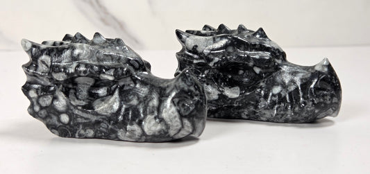 Two small carved stone dragon heads, likely made of marbled black and white stone, displayed on a white surface against a light gray marble-patterned background.